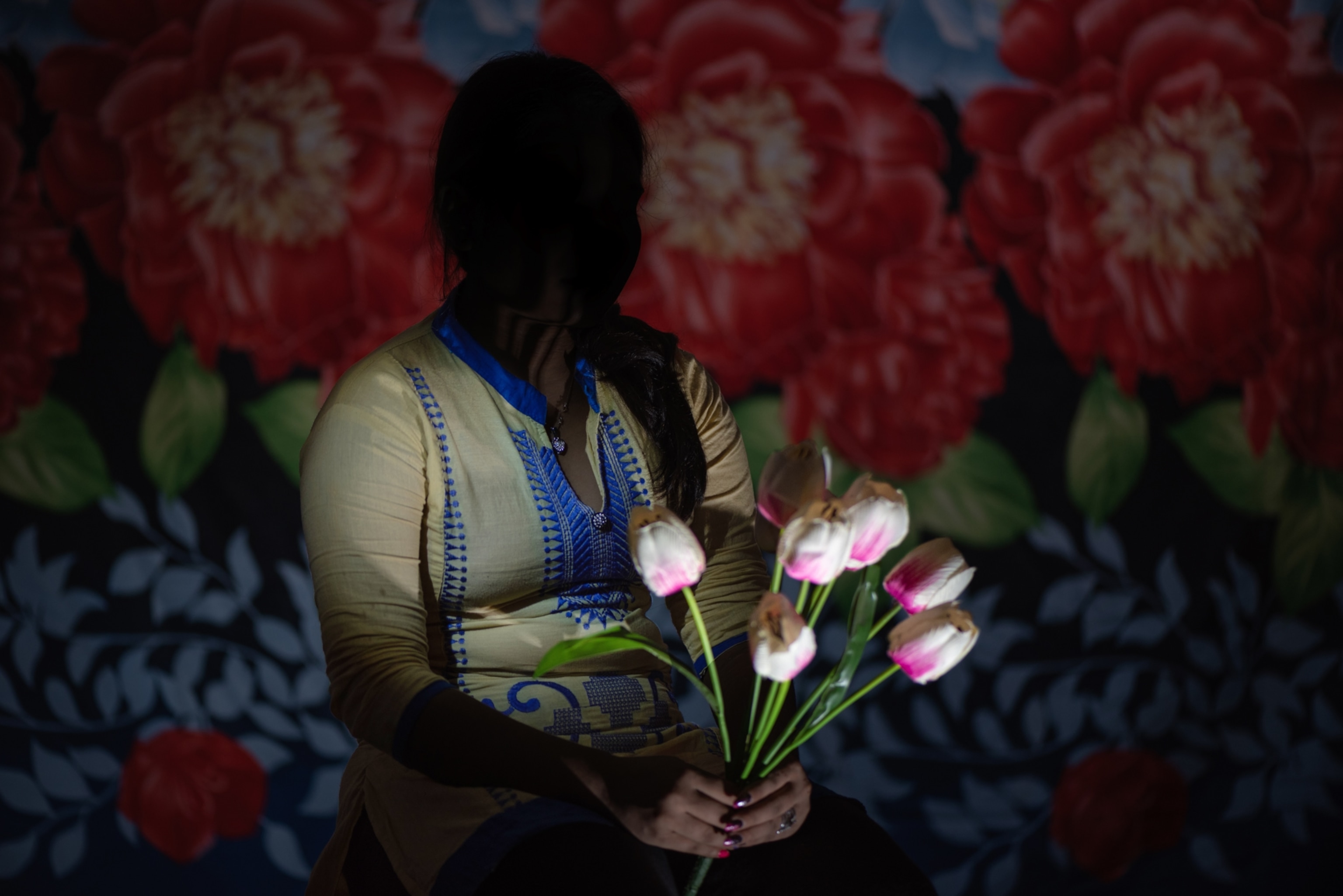 a girl holding light pink tulips with her face silhouetted against a patterned wall