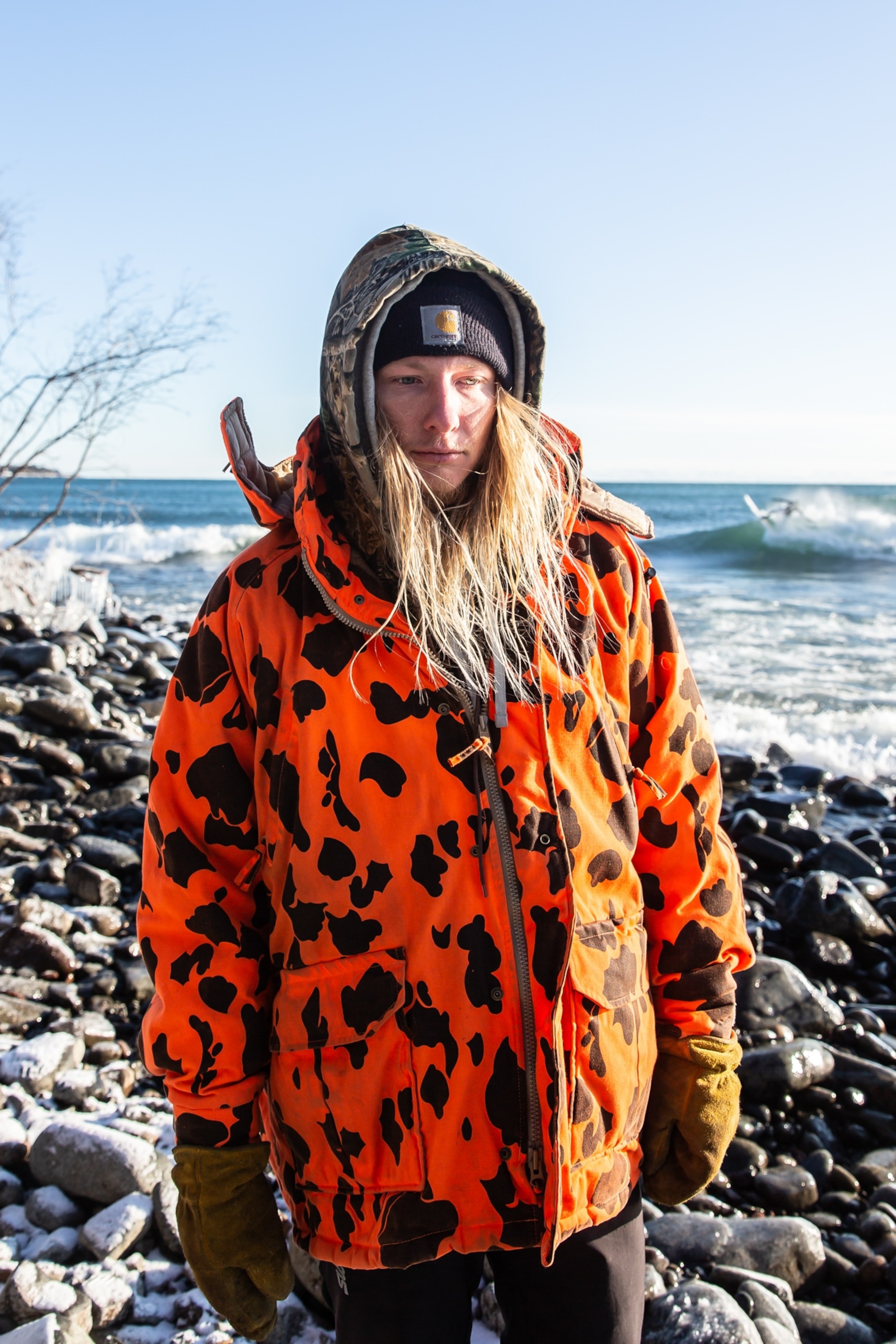 a young man with long blonde hair, wearing a bright orange printed jacked