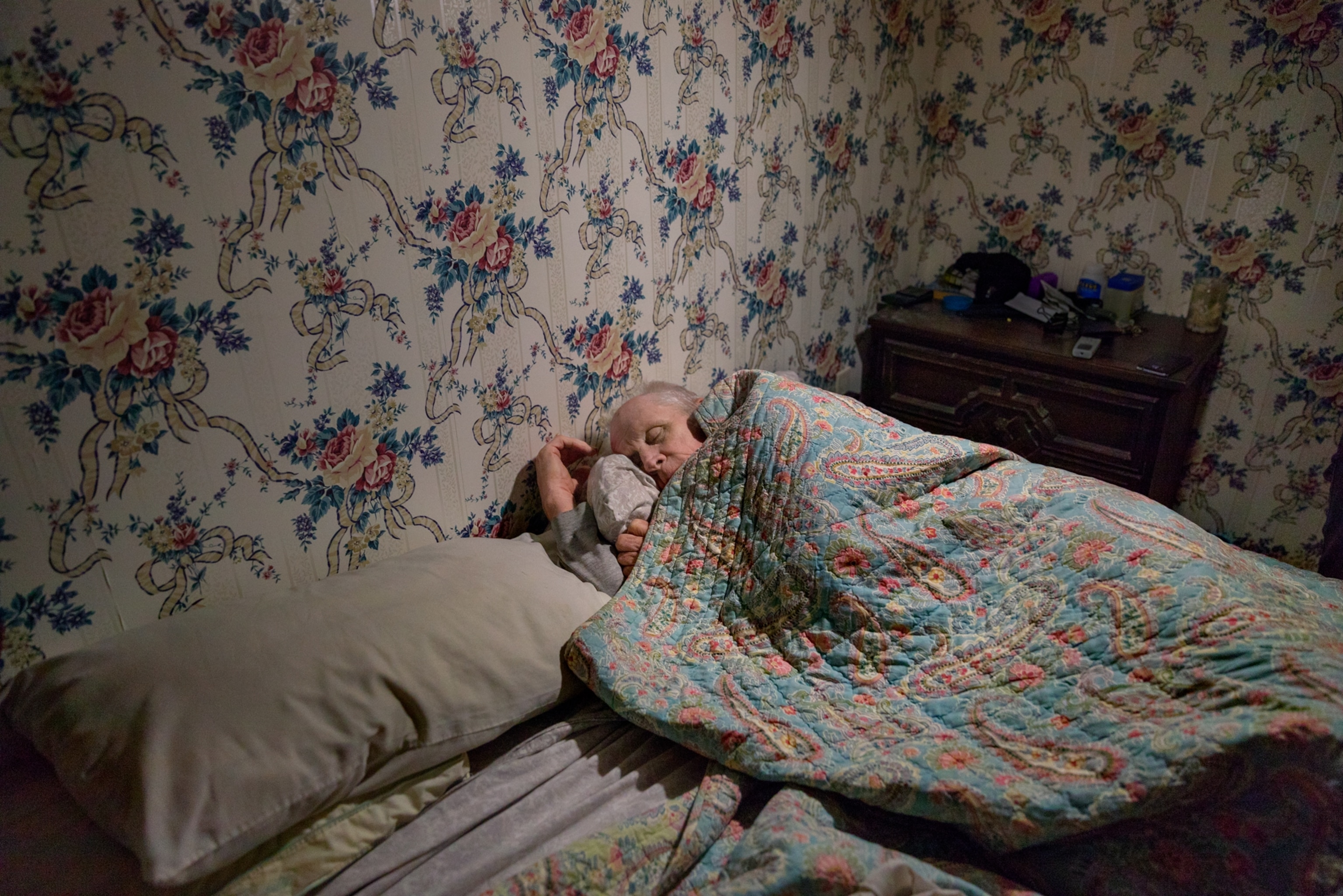 a man sleeping in bed under a floral blanket surrounded by walls with floral wallpaper