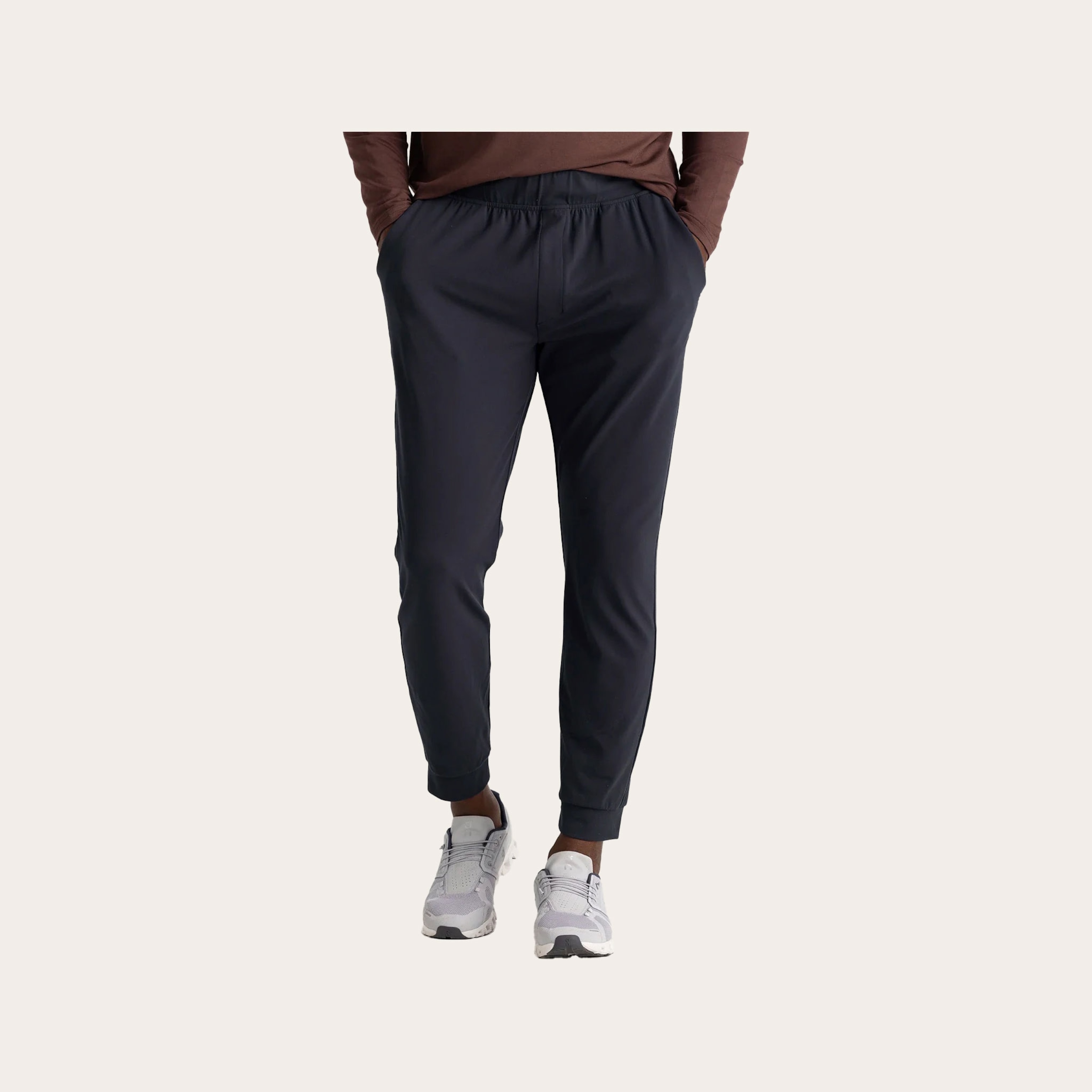 Man wearing black joggers in front of a tan background.