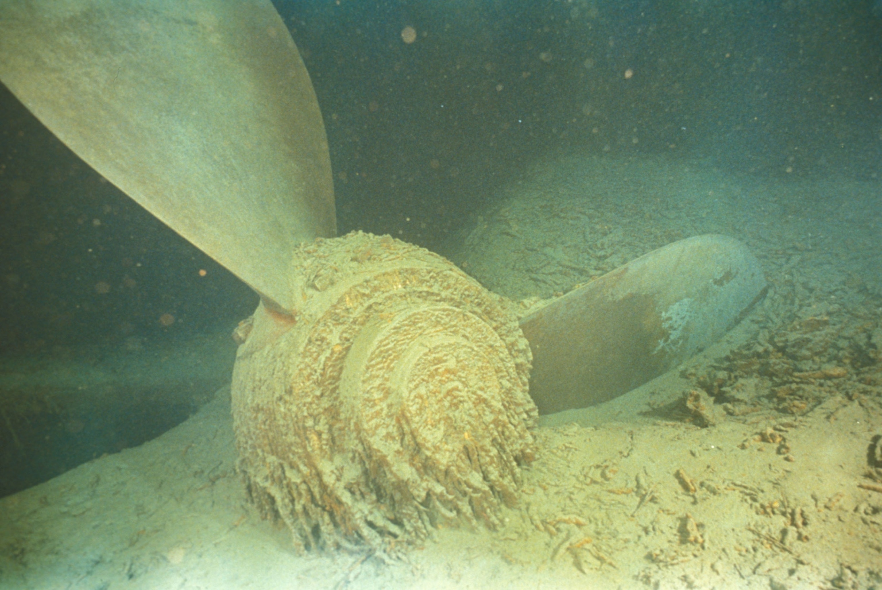 Propeller covered in sand and debris sits at the bottom of the ocean floor.
