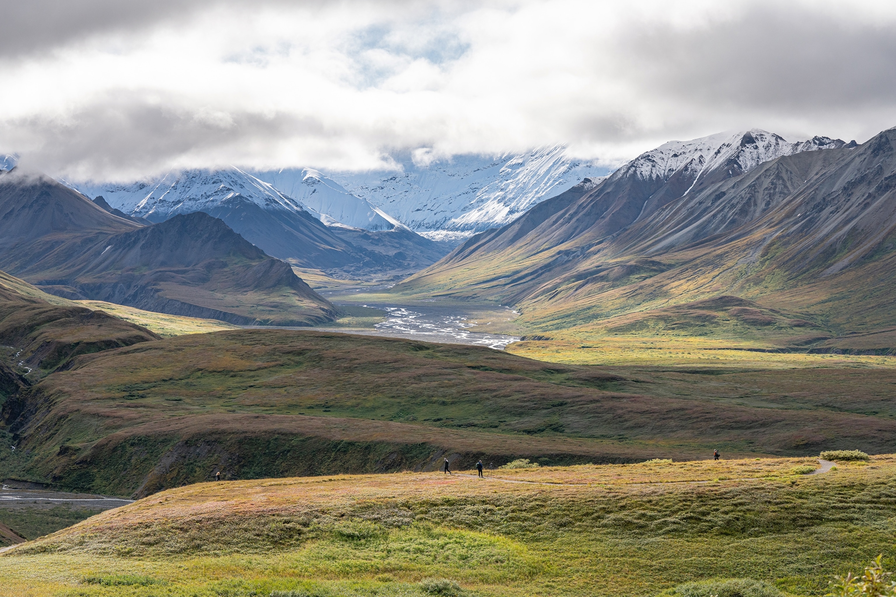 A landscape shot over a wide field valley with a mountain ridge in the background shrouded in clouds.