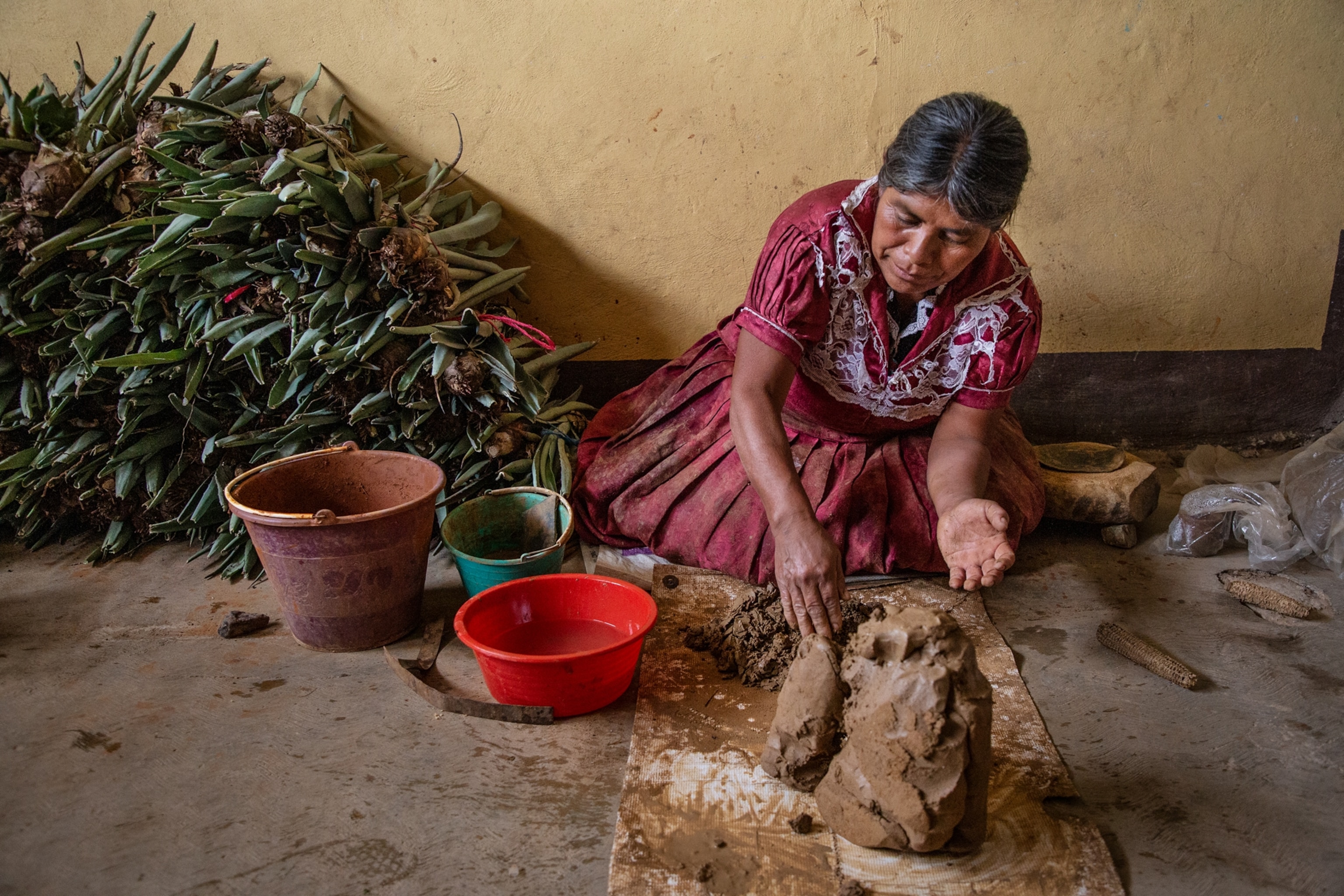 a woman kneads clay and sand to prepare the mixture for the creation of red pottery pieces