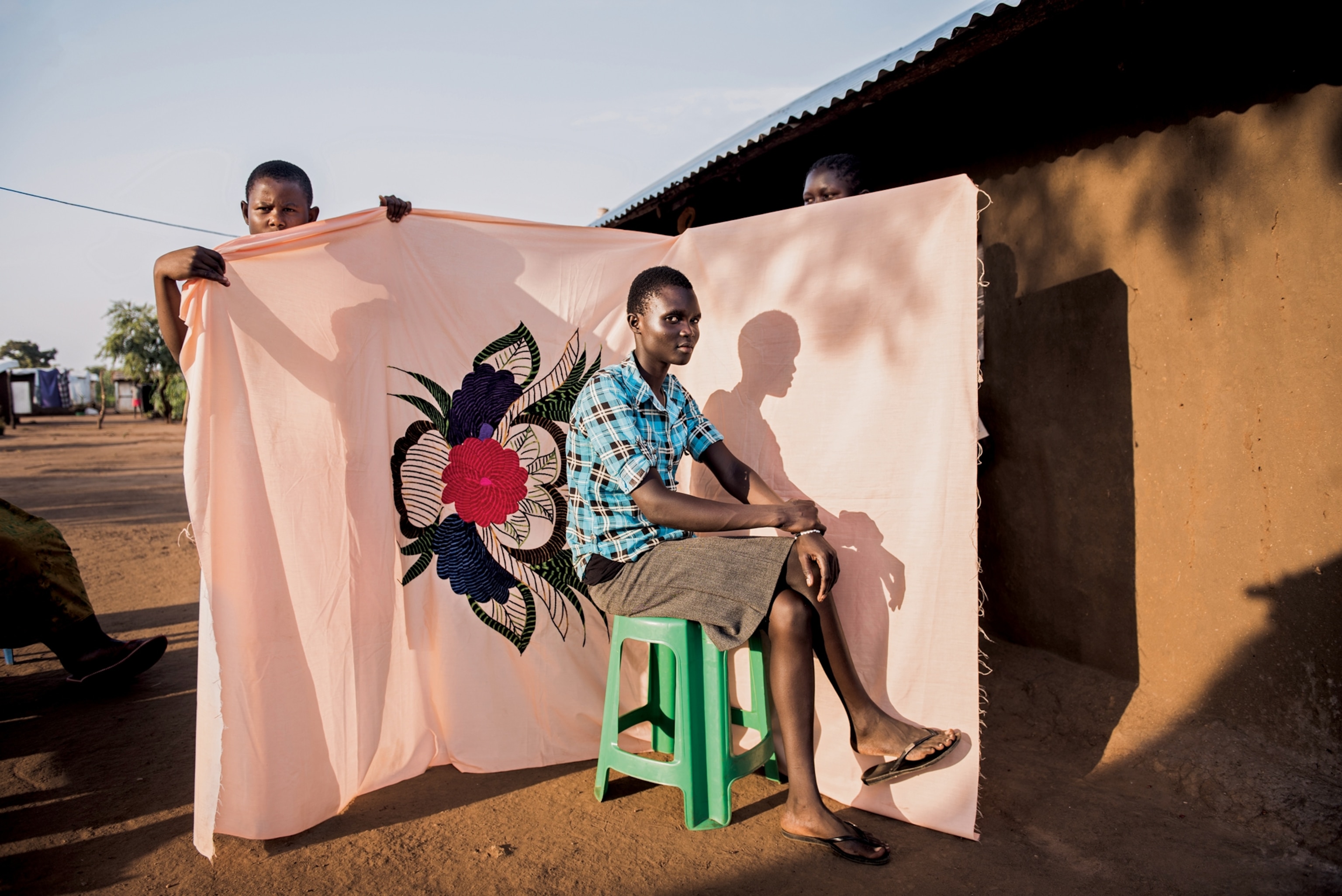 young women posing in front of pink bedsheets with colorful flowers embroidered on it.