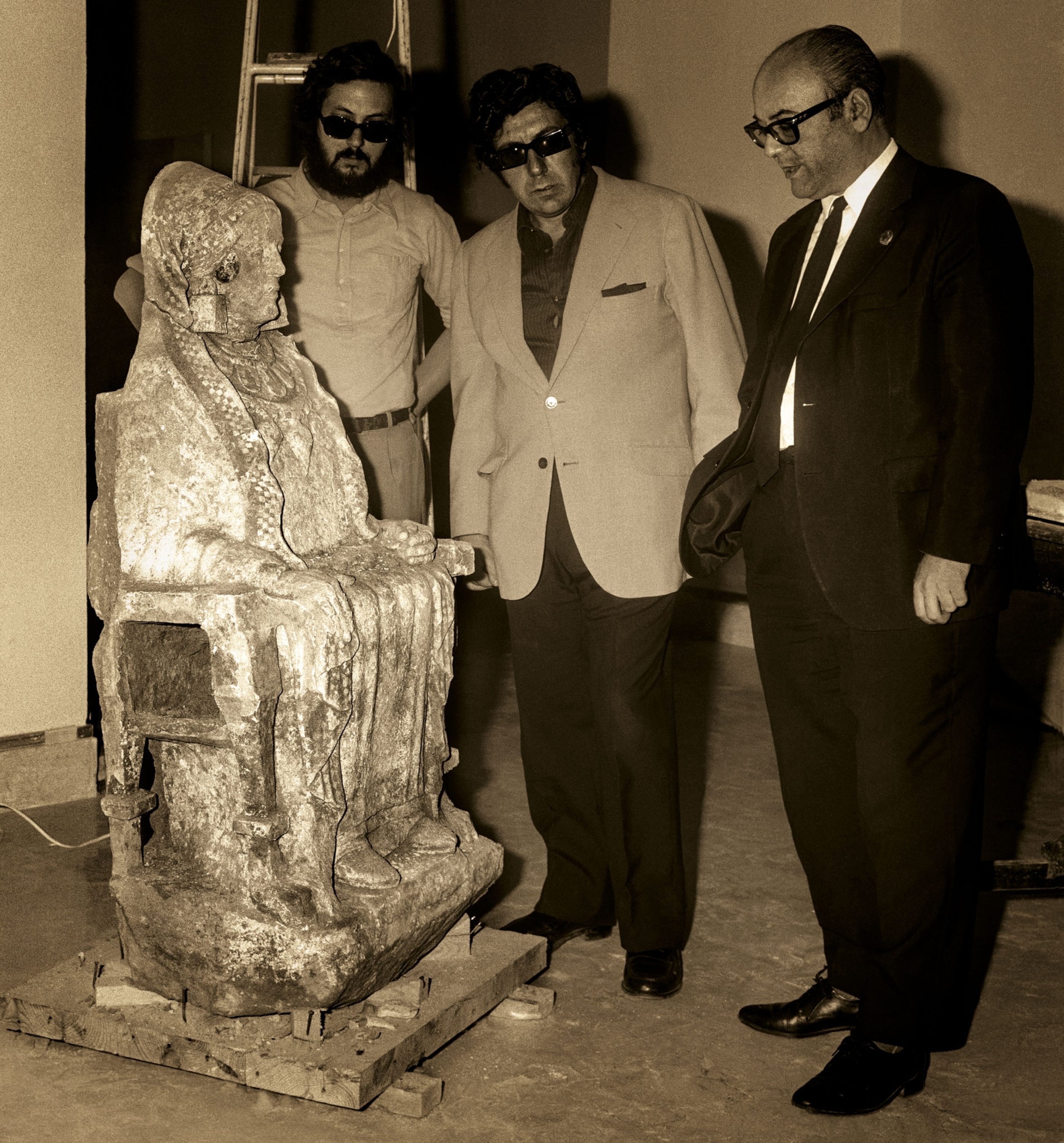 Three men look at a statue of a seated woman