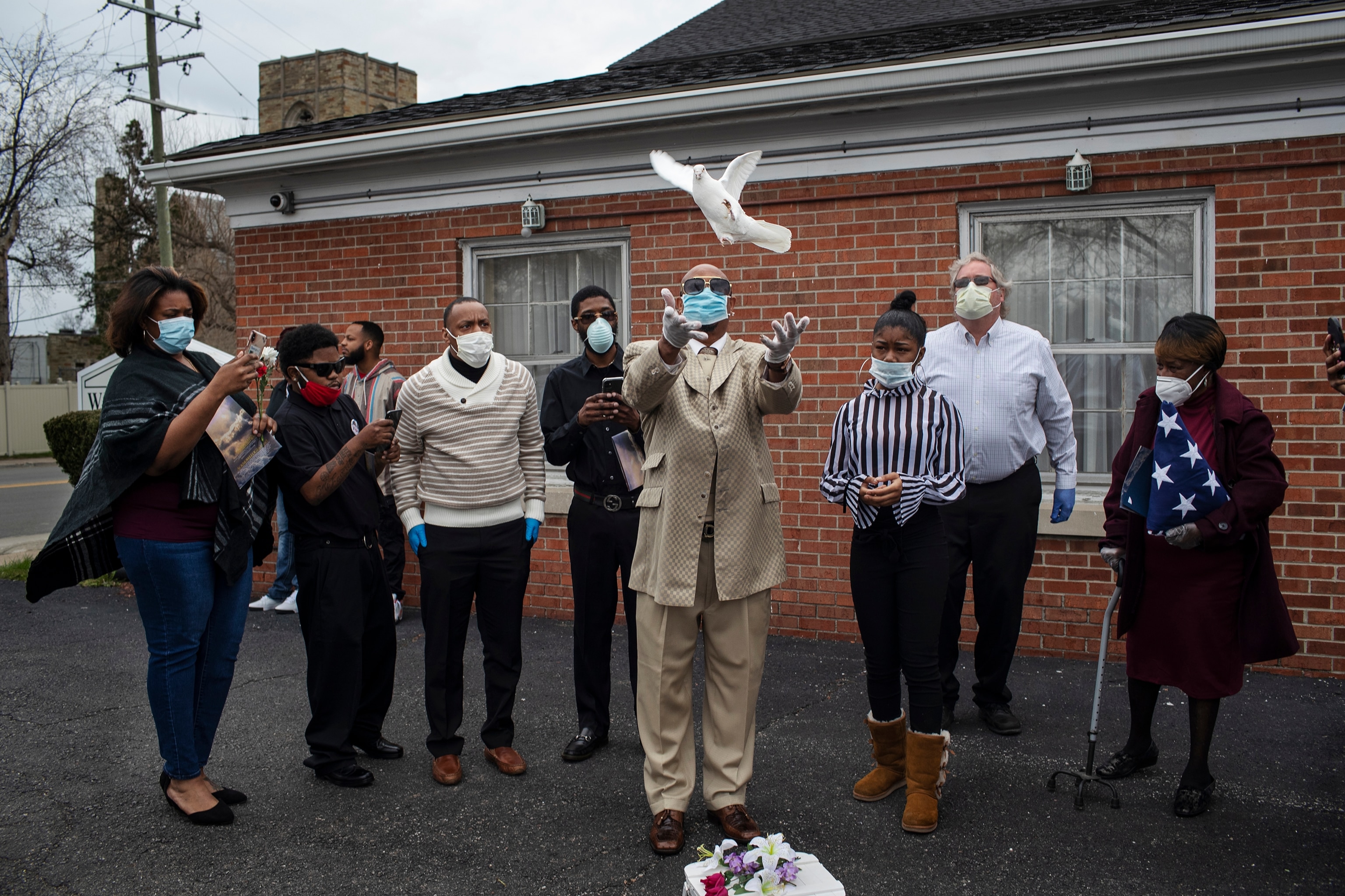funeral attendees watching as a man releases a dove