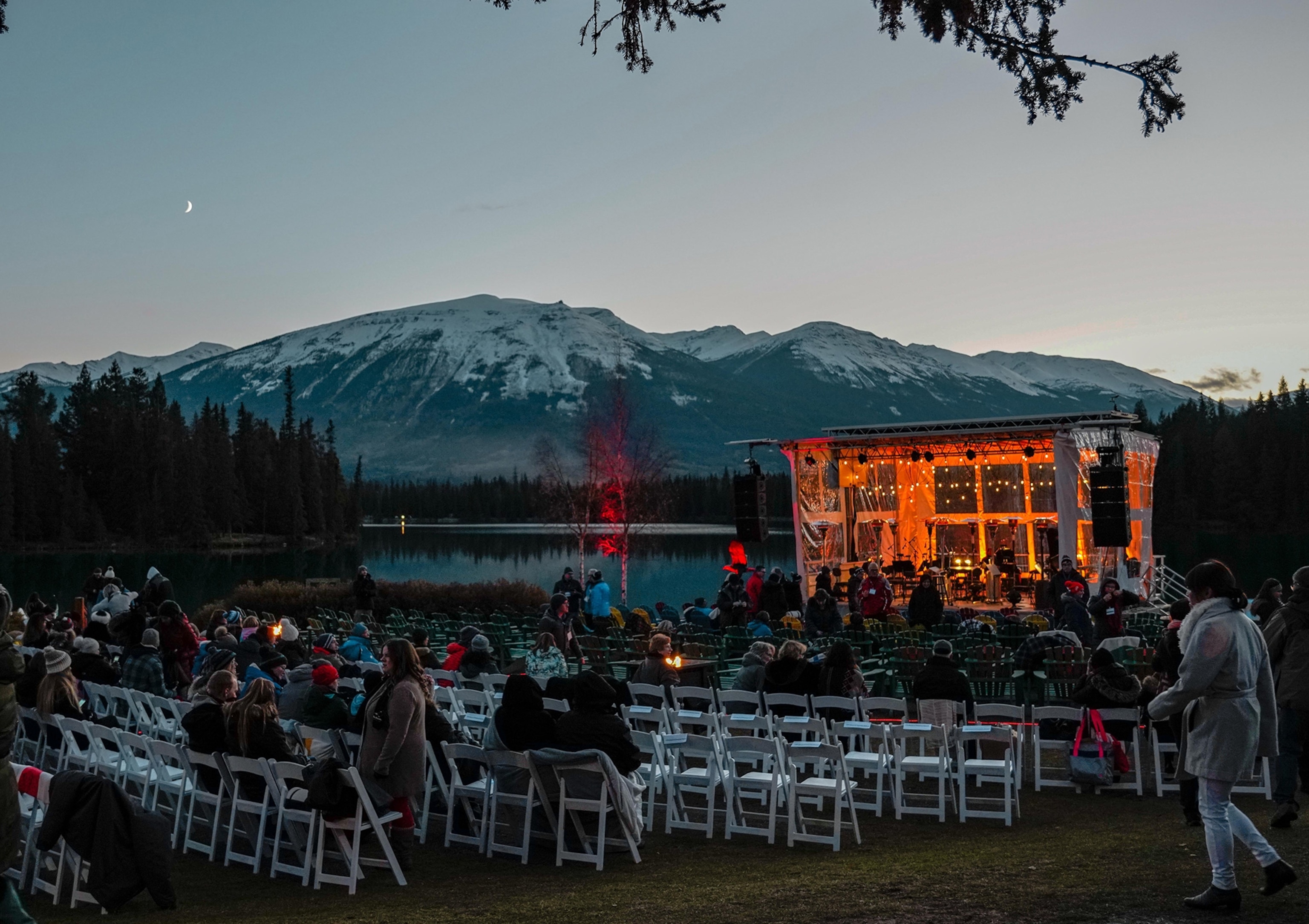 People take their seats for an outdoor night performance with the mountains in the background.