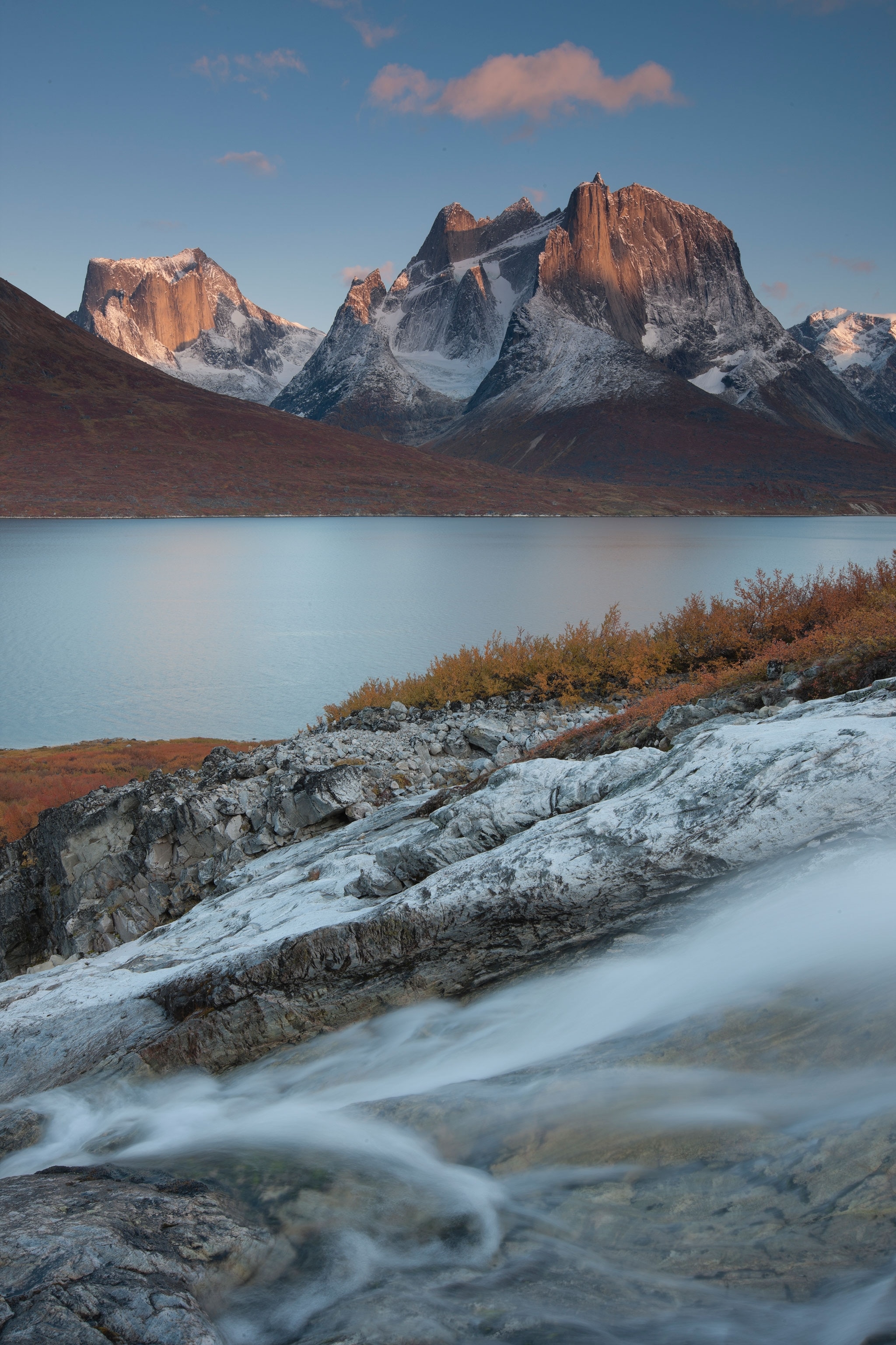 Water streams are blurred in the foreground of the image; a larger body of water separates a larger mountain in the background.