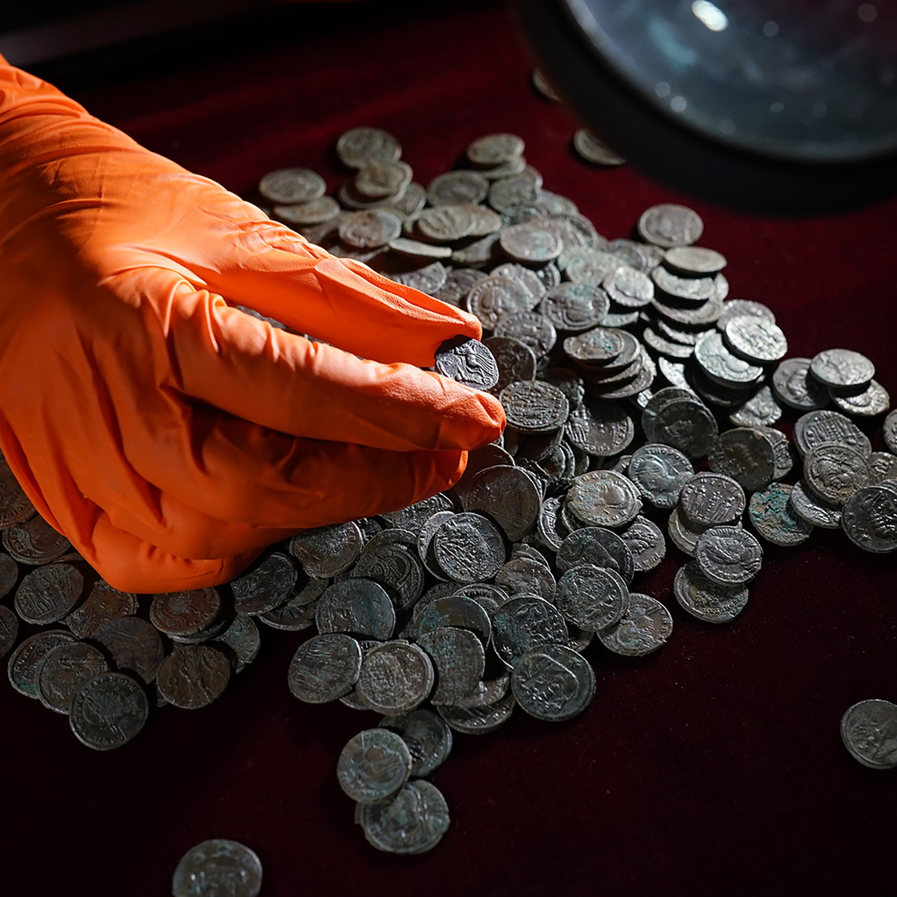 An orange gloved hand hold a Roman coin on display at the British Museum in London.