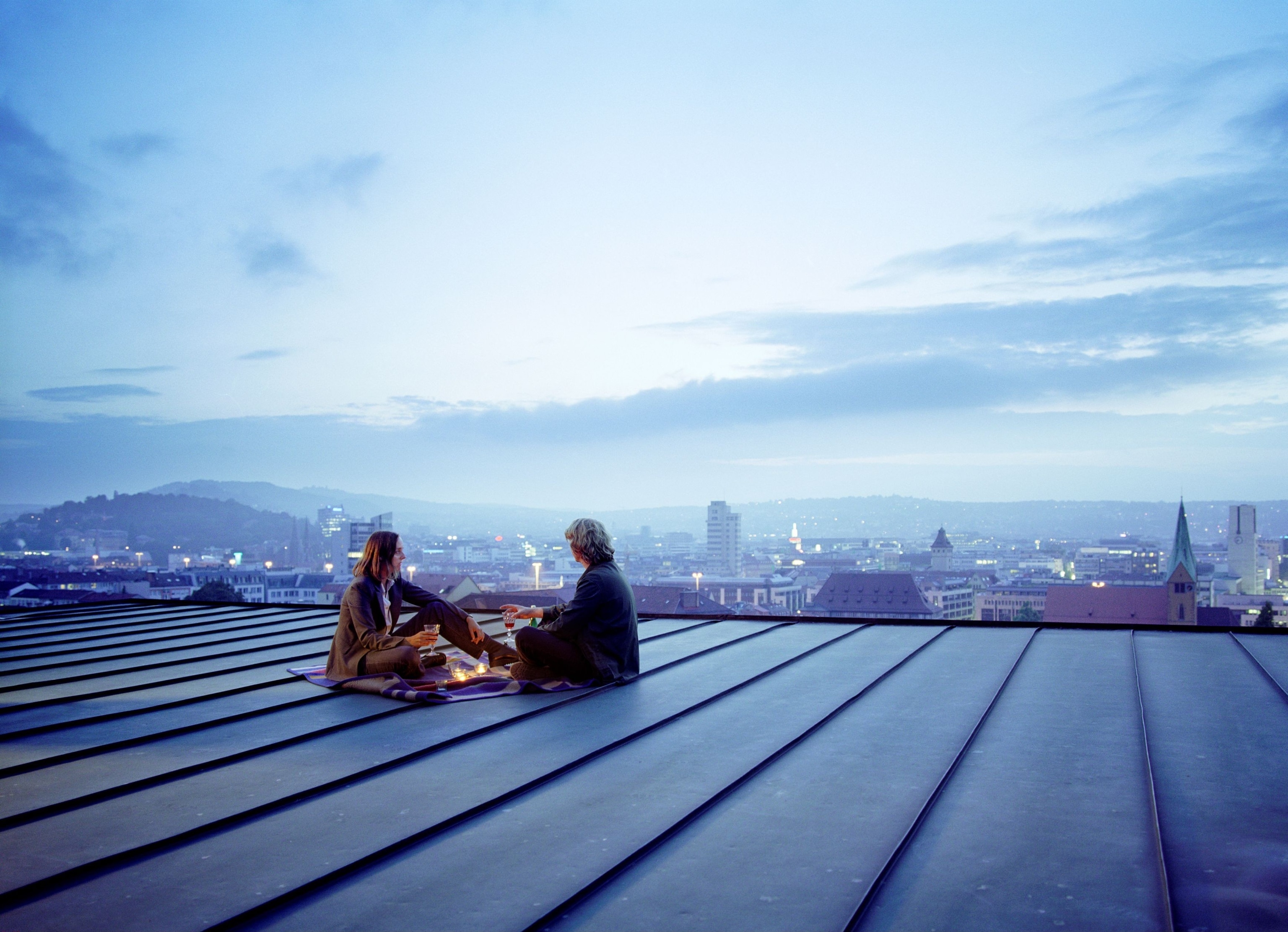 Young couple sit on top of a roof, looking over the city in Stuttgart, Germany
