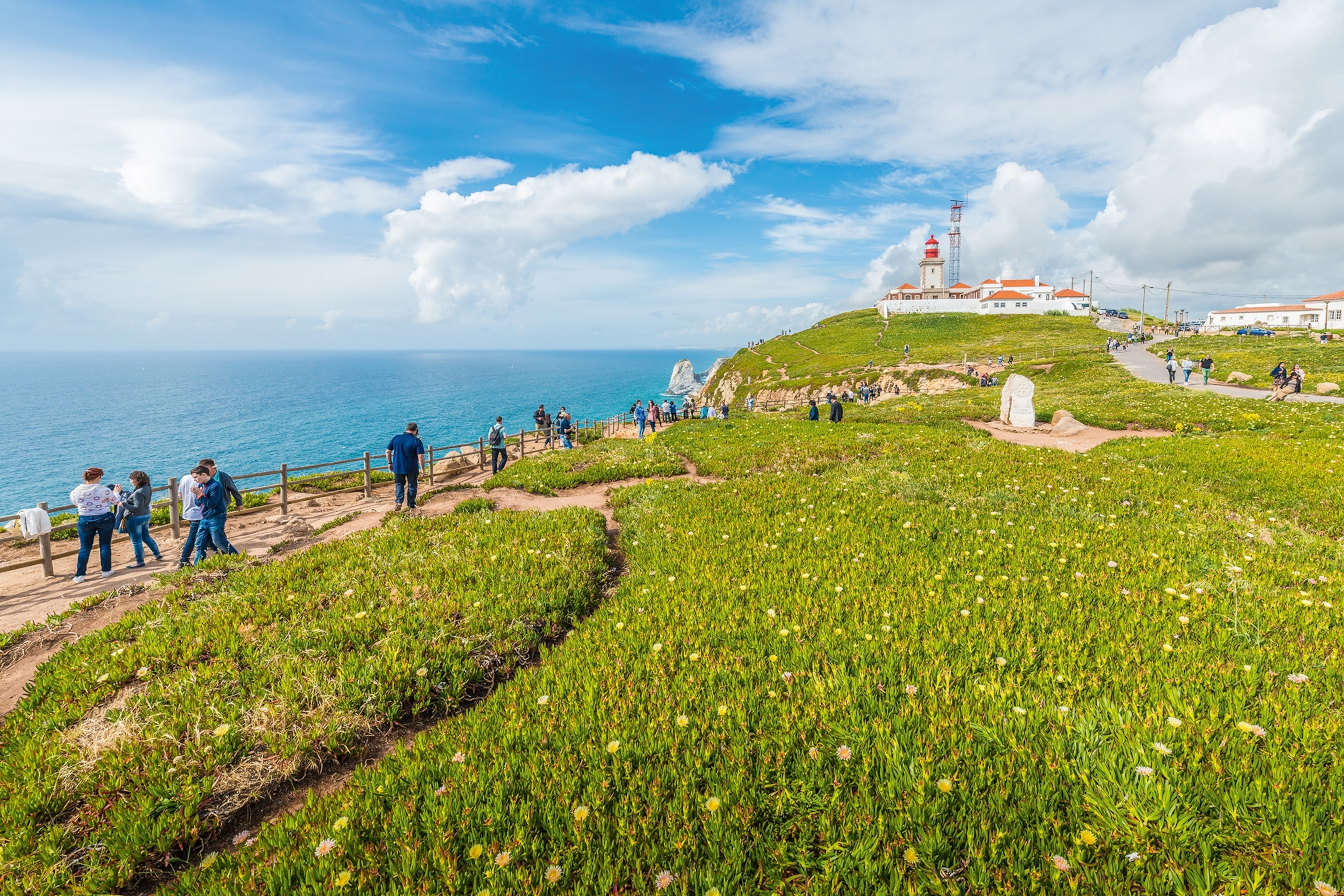 People walking along a fence on a cliffside overlooking the sea