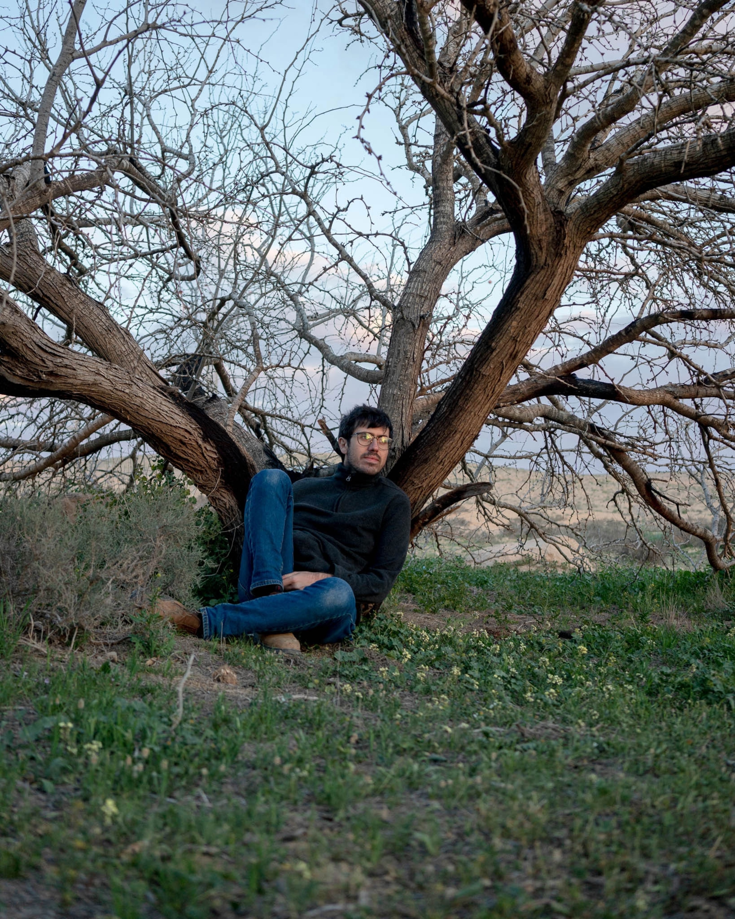 a man poses for a portrait in the spindly branches of an acacia tree