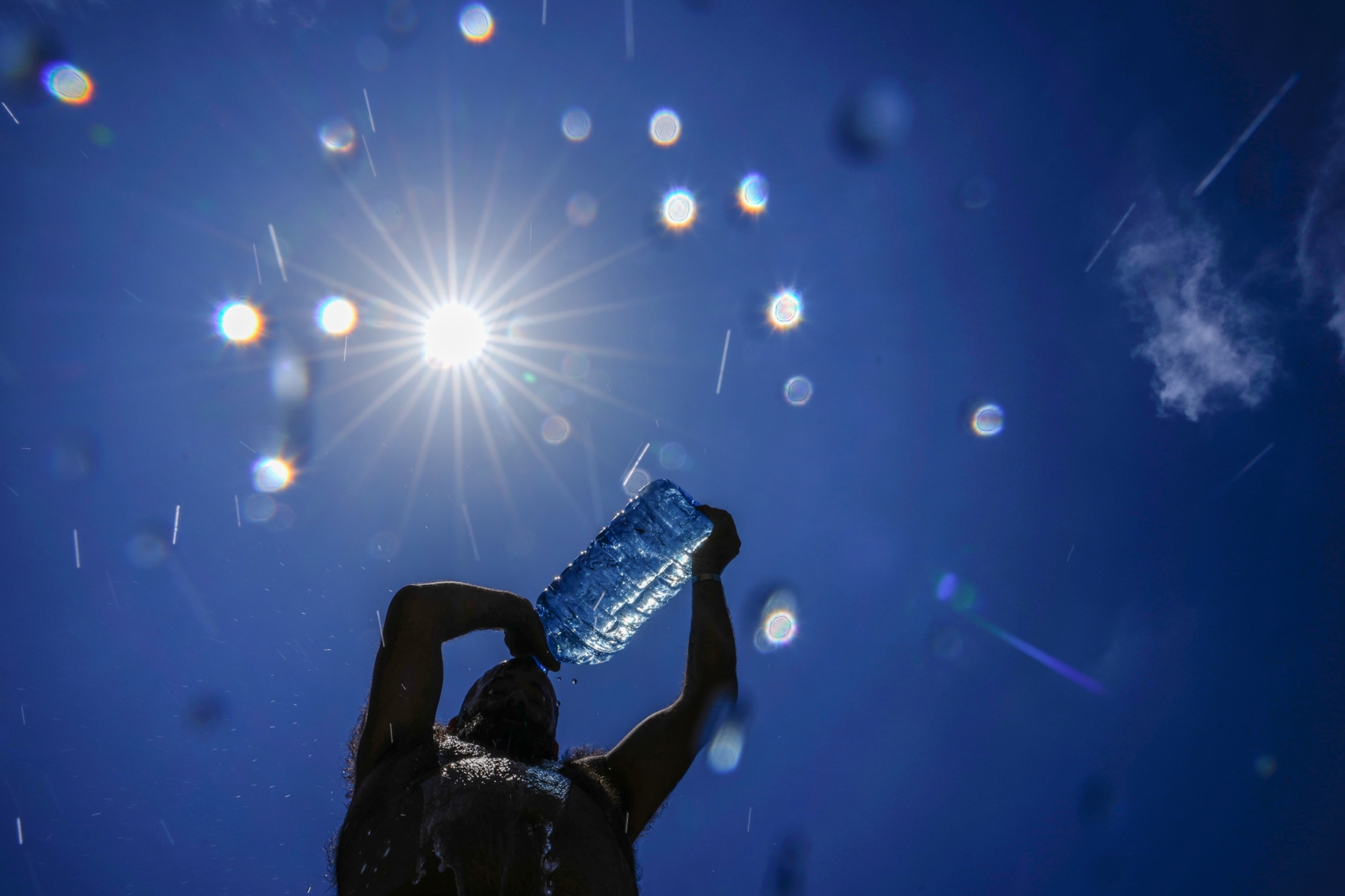 A man silhouetted as he pours water onto his head.