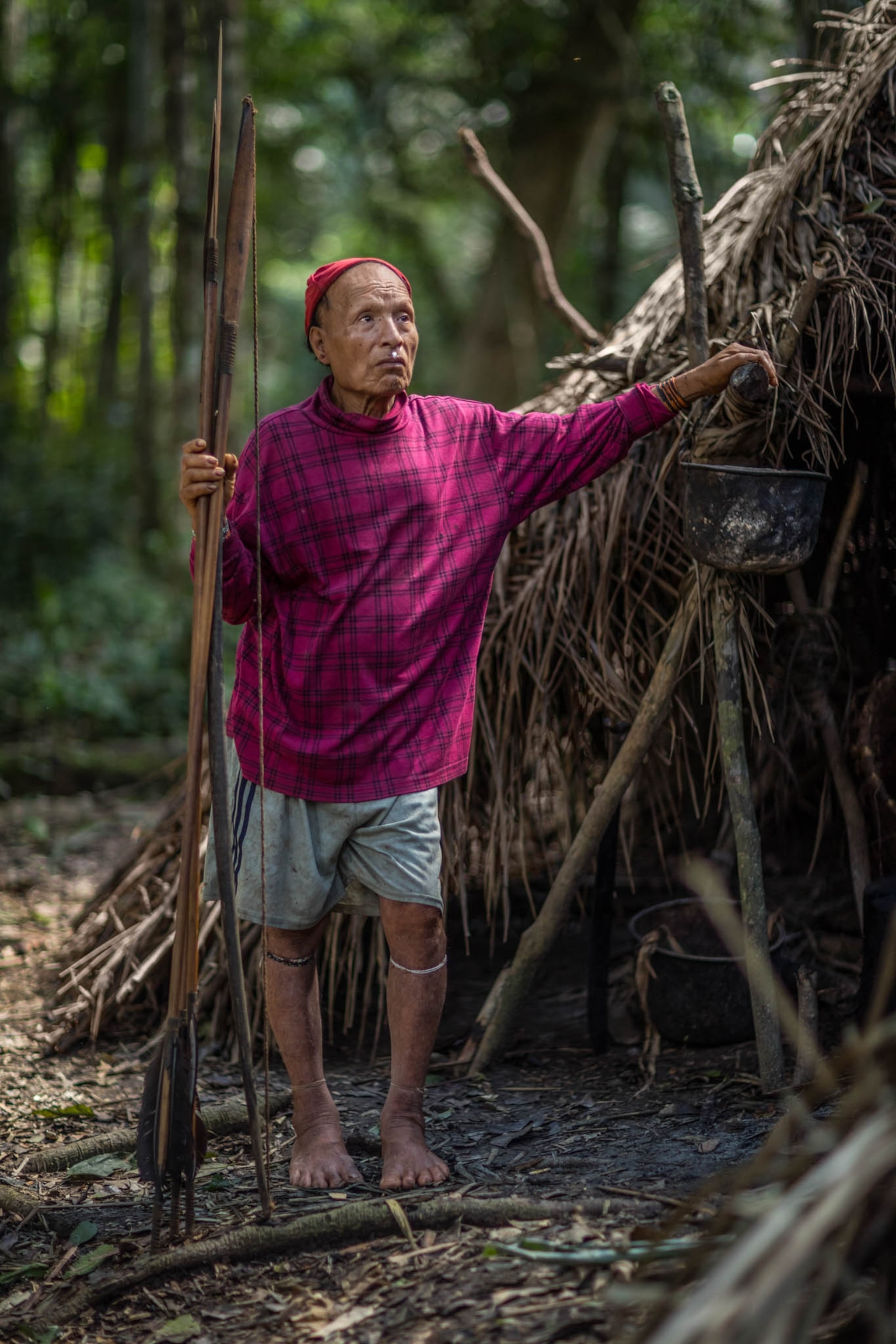 a man wearing a plaid shirt holding areas and leaning on a hut