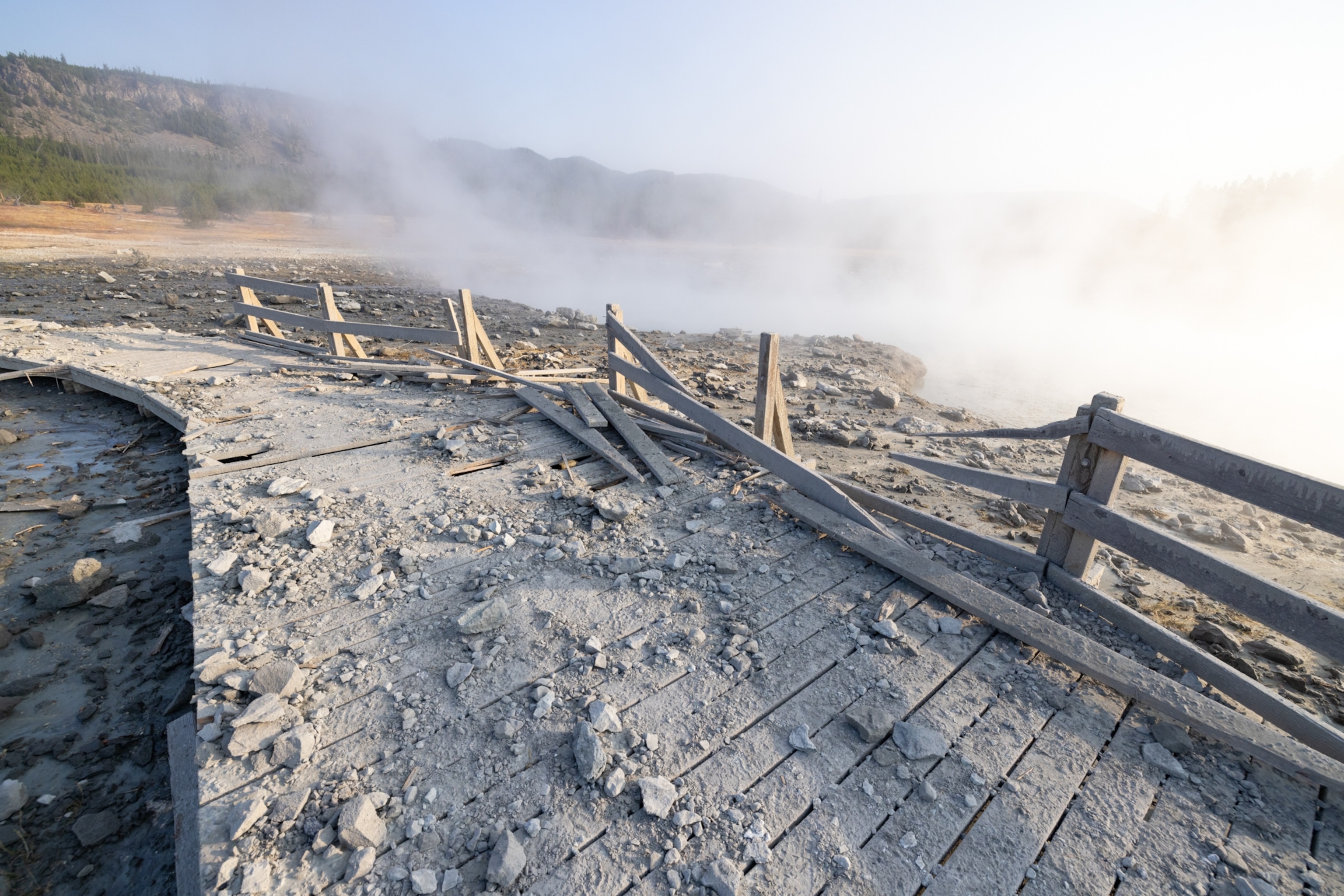 A section of boardwalk covered in rocks and dust. The wooden railings have been blown apart by the force of a recent hydrothermal explosion.