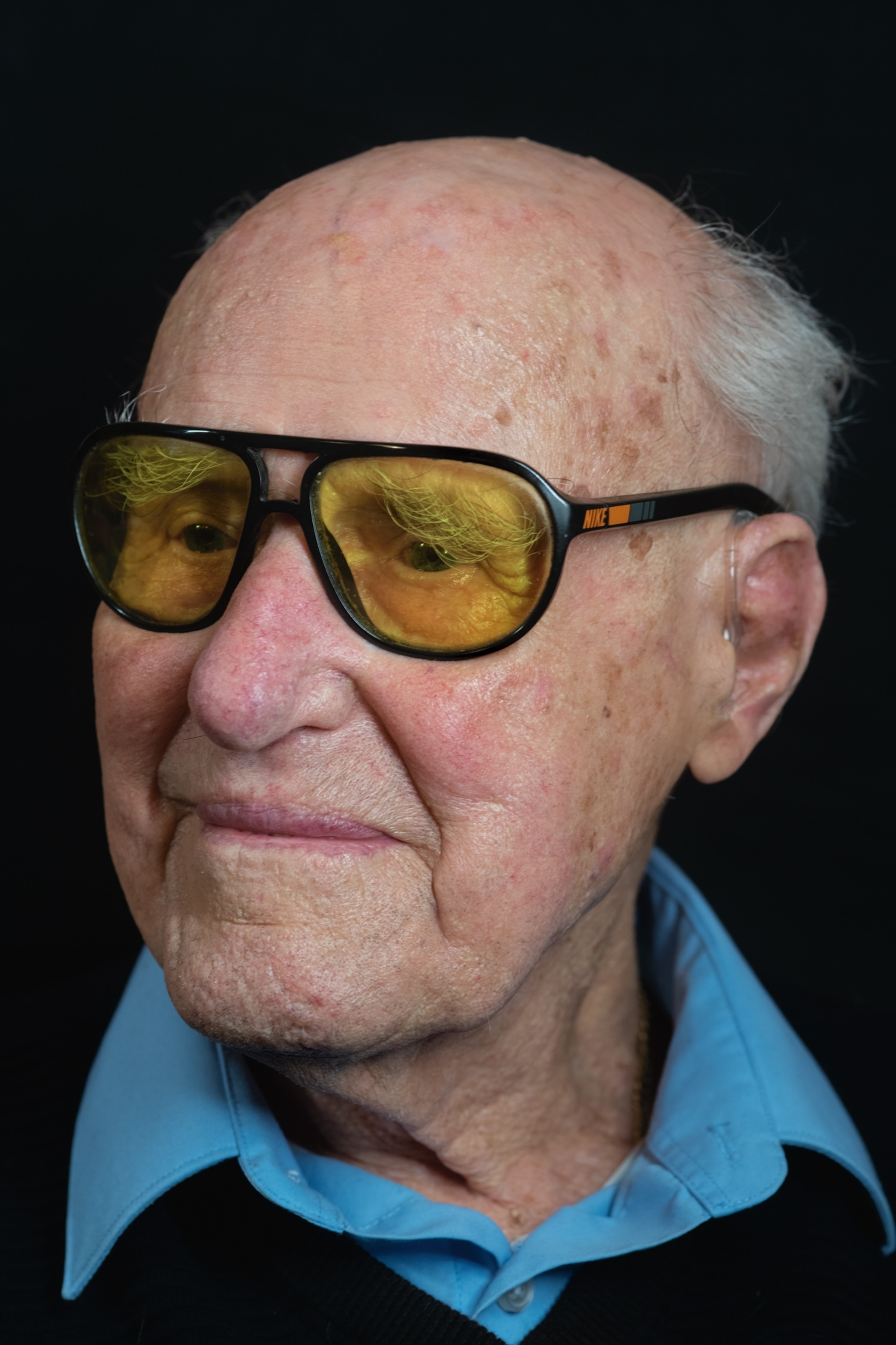 an older man wearing yellow glasses standing for a portrait