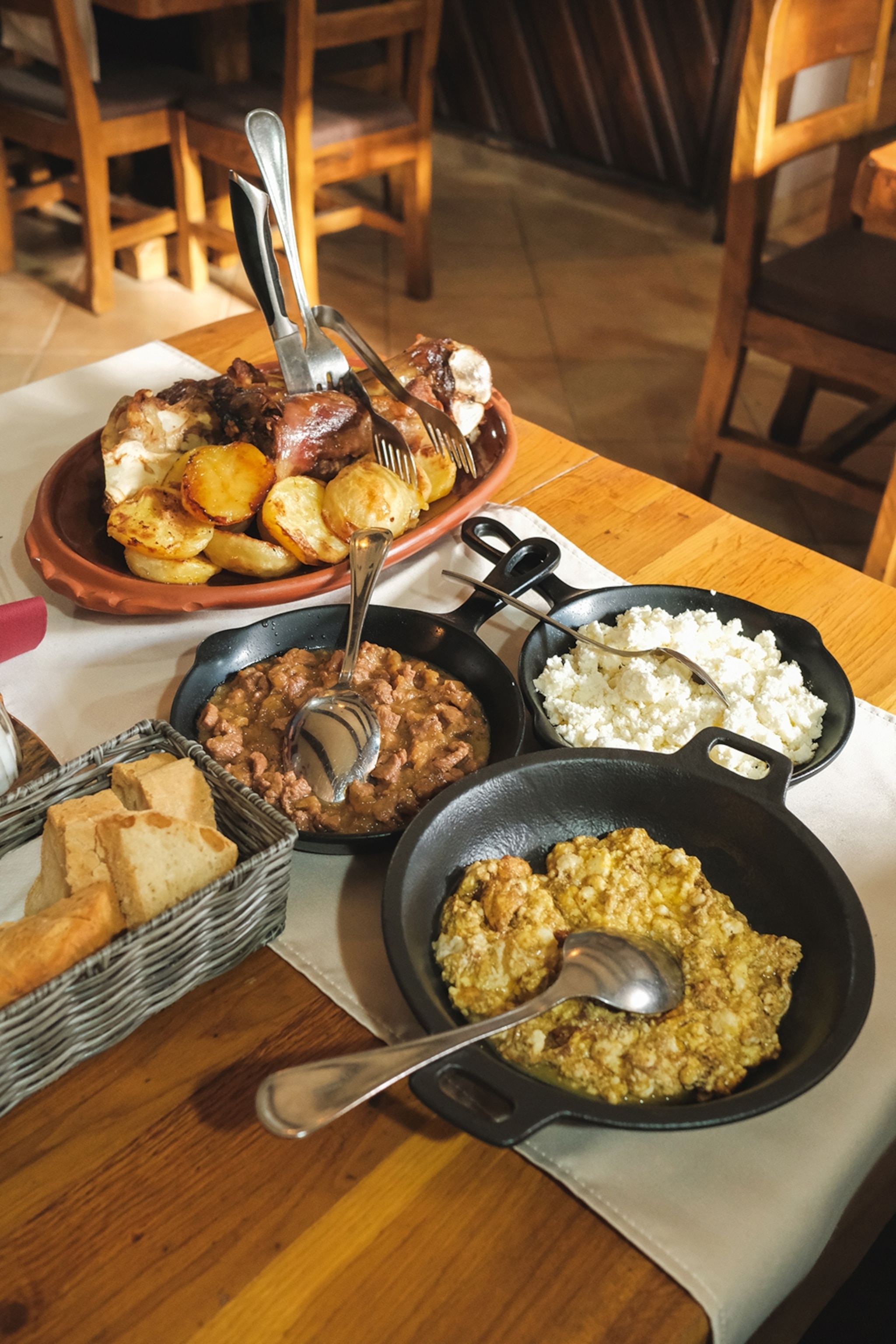 Stews, meat, potatoes and chunks of bread served in bowls and baskets on a table.