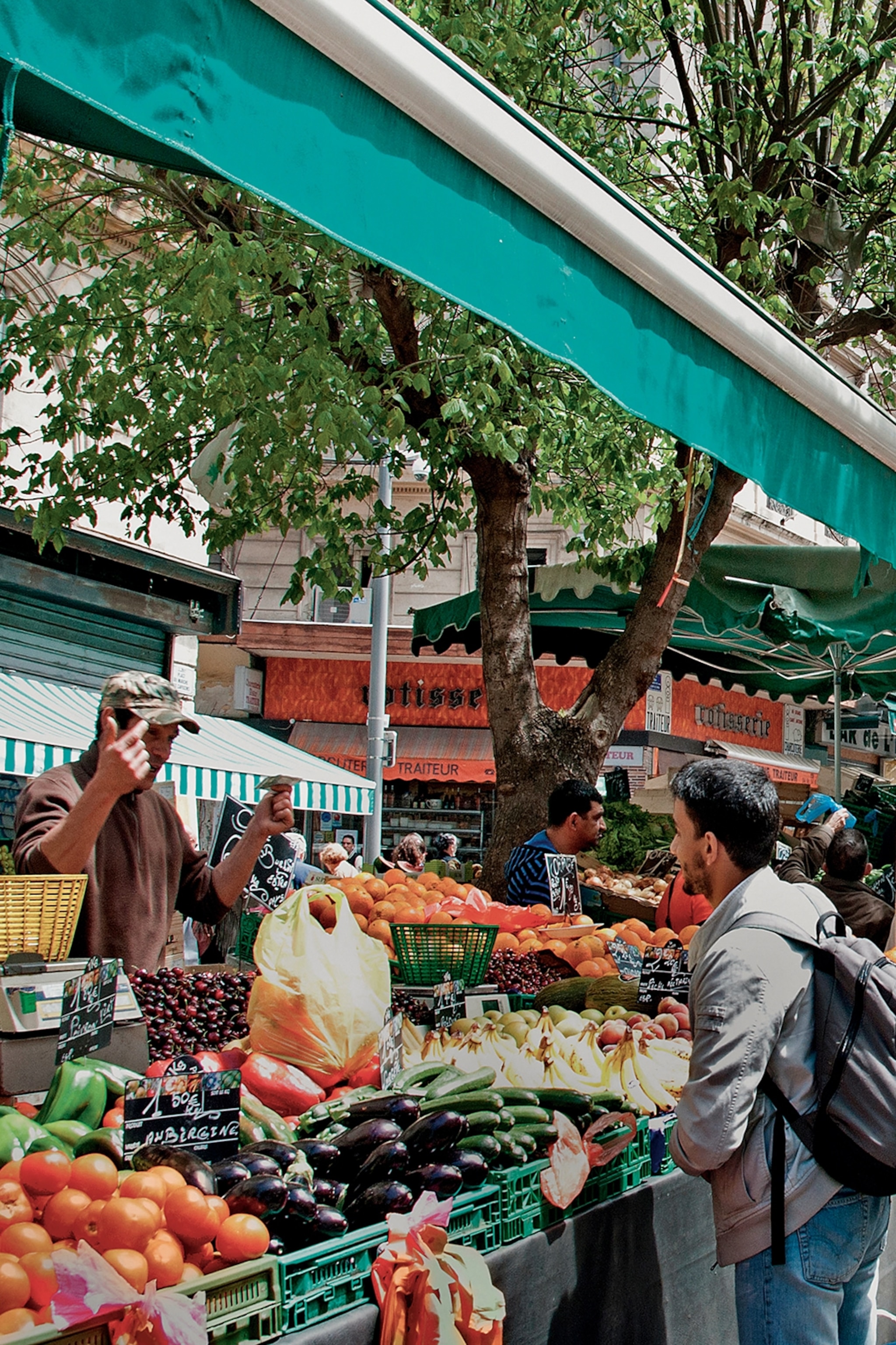 Two men, one seller and one buyer, haggling across a fruit and vegetable stall on a market in Marseille.