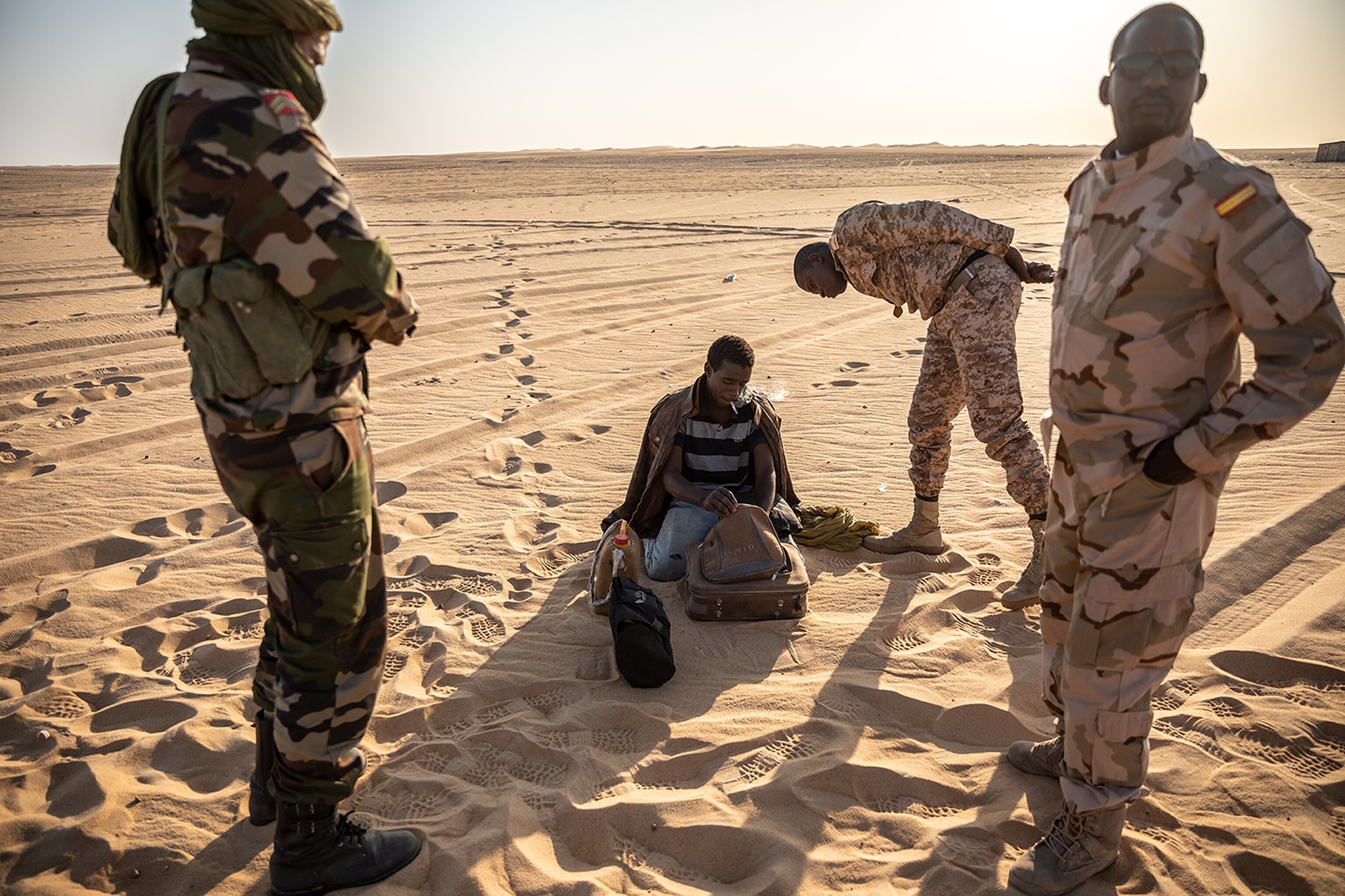 soldiers speaking with a man opening a backpack in the desert
