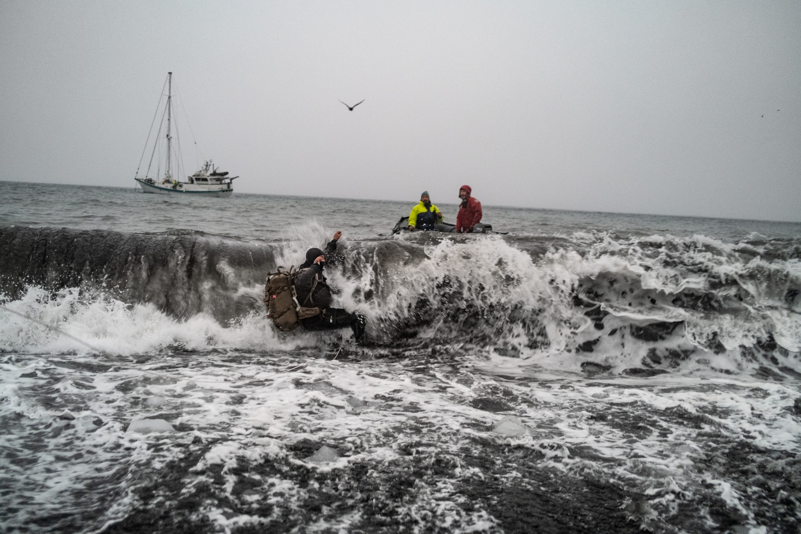 Two people in the boat helping another one in the sea waves.