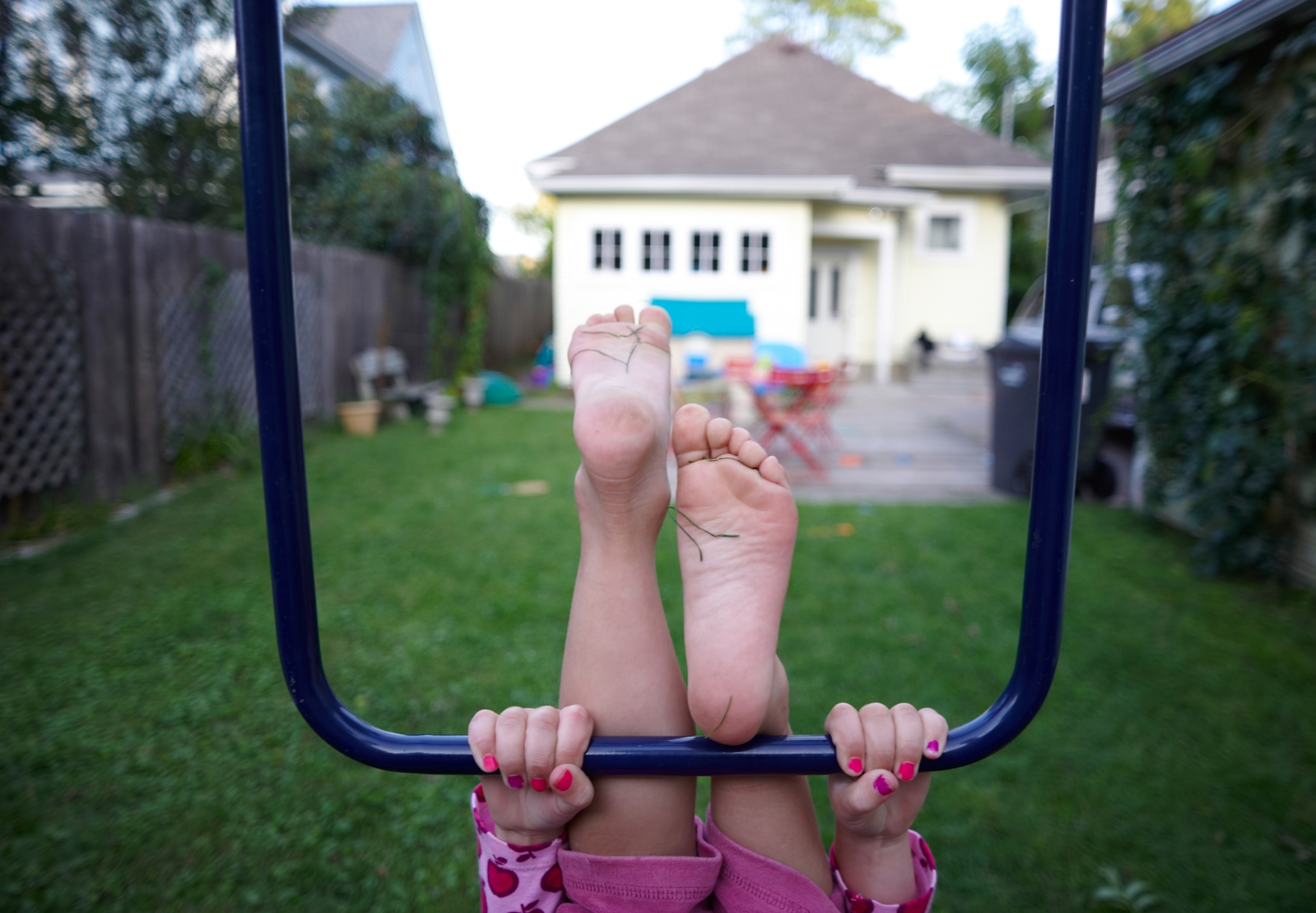 A girl hangs upside down from the monkey bars in her backyard.