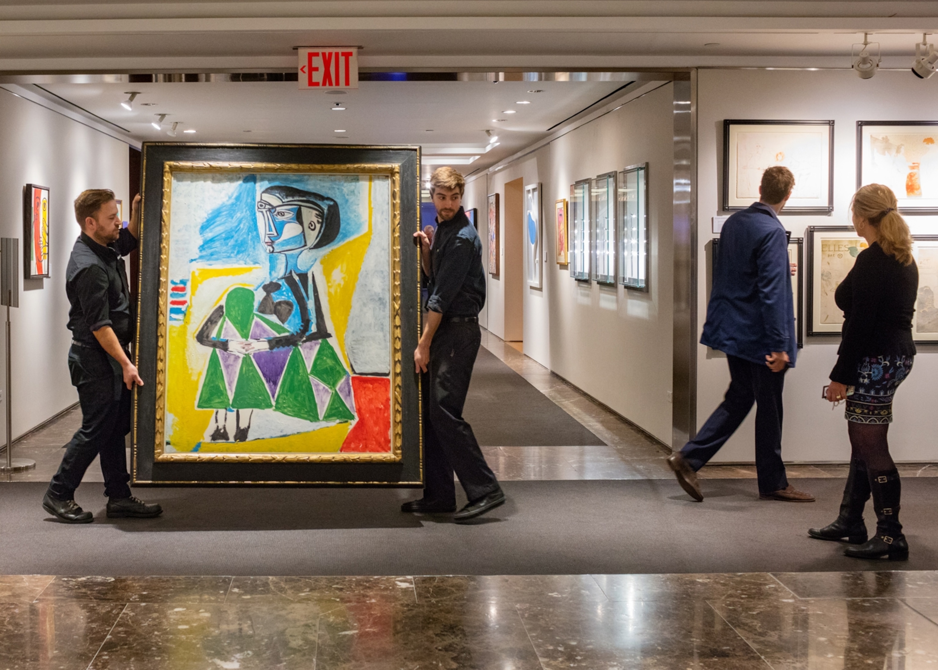 two men holding and walking with a colorful Picasso painting inside an auction house