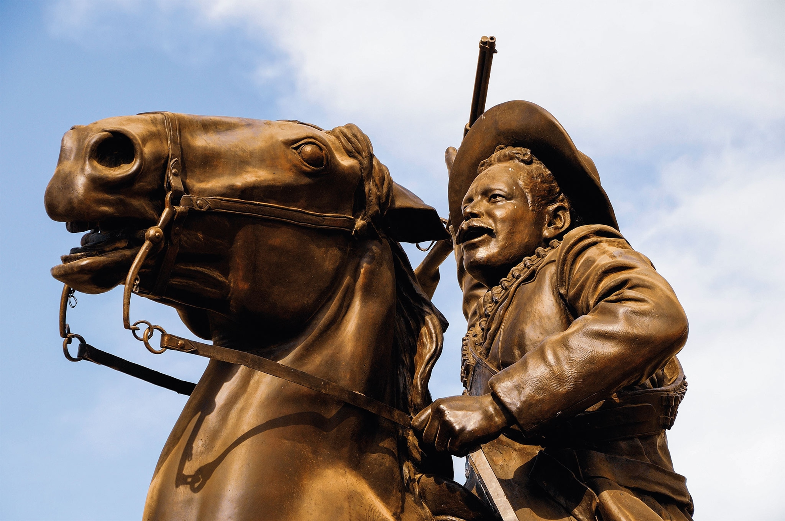 A bronze statue of a man with a hat and gun riding a horse