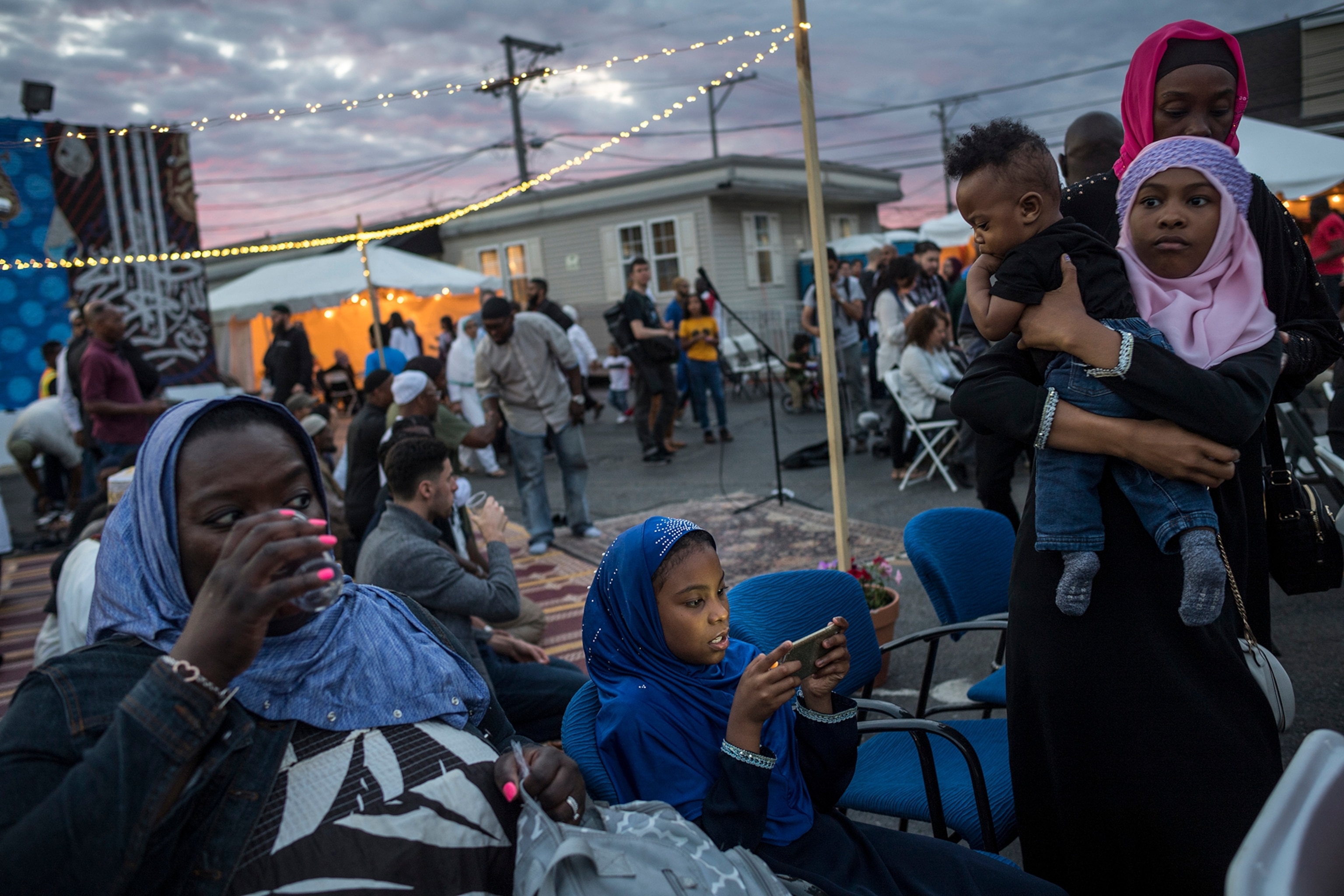 a young girl playing on a cellphone as her family stands and sits around her