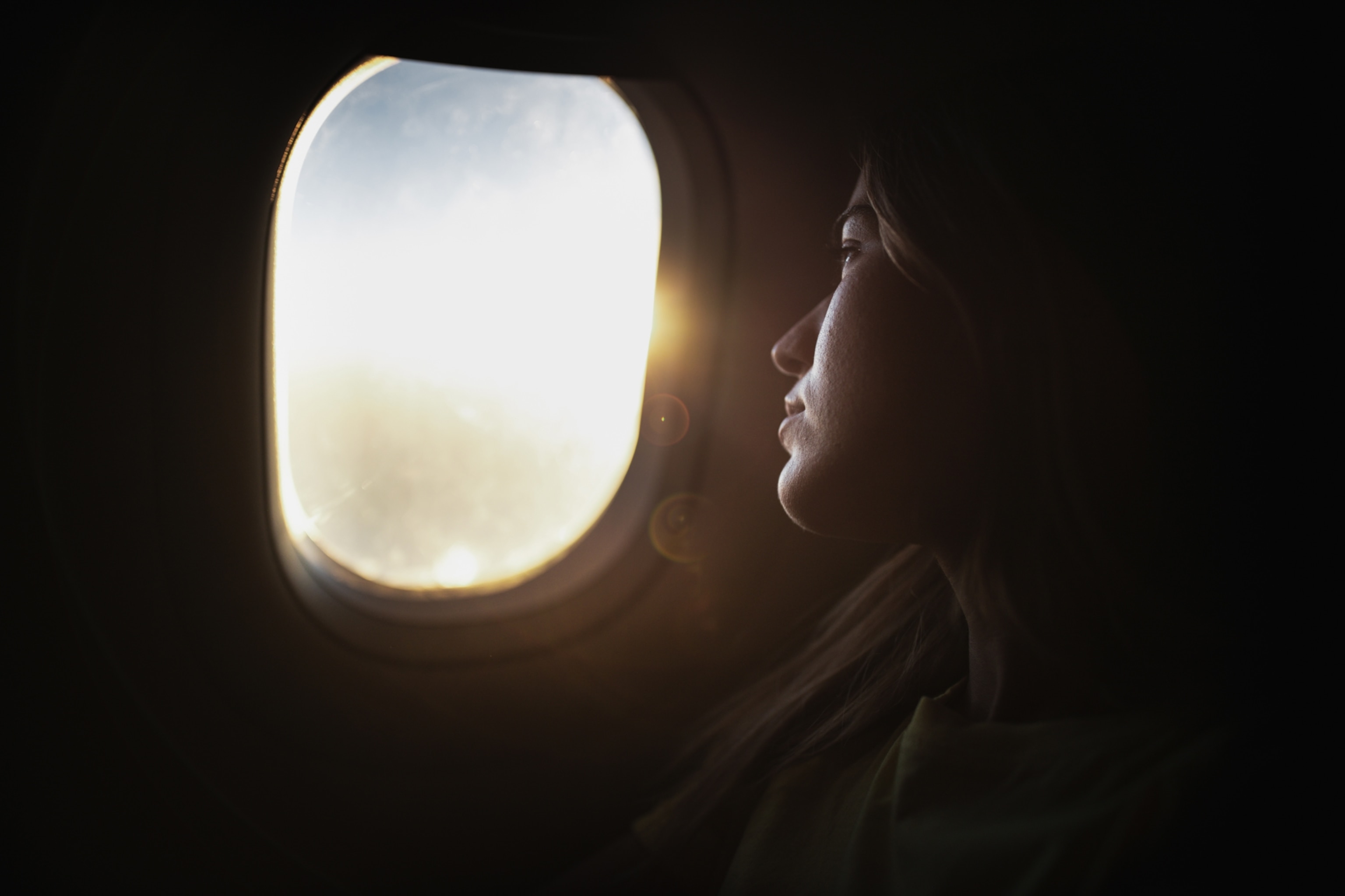 A woman's face, lit by soft, warm light as she looks out an airplane window.
