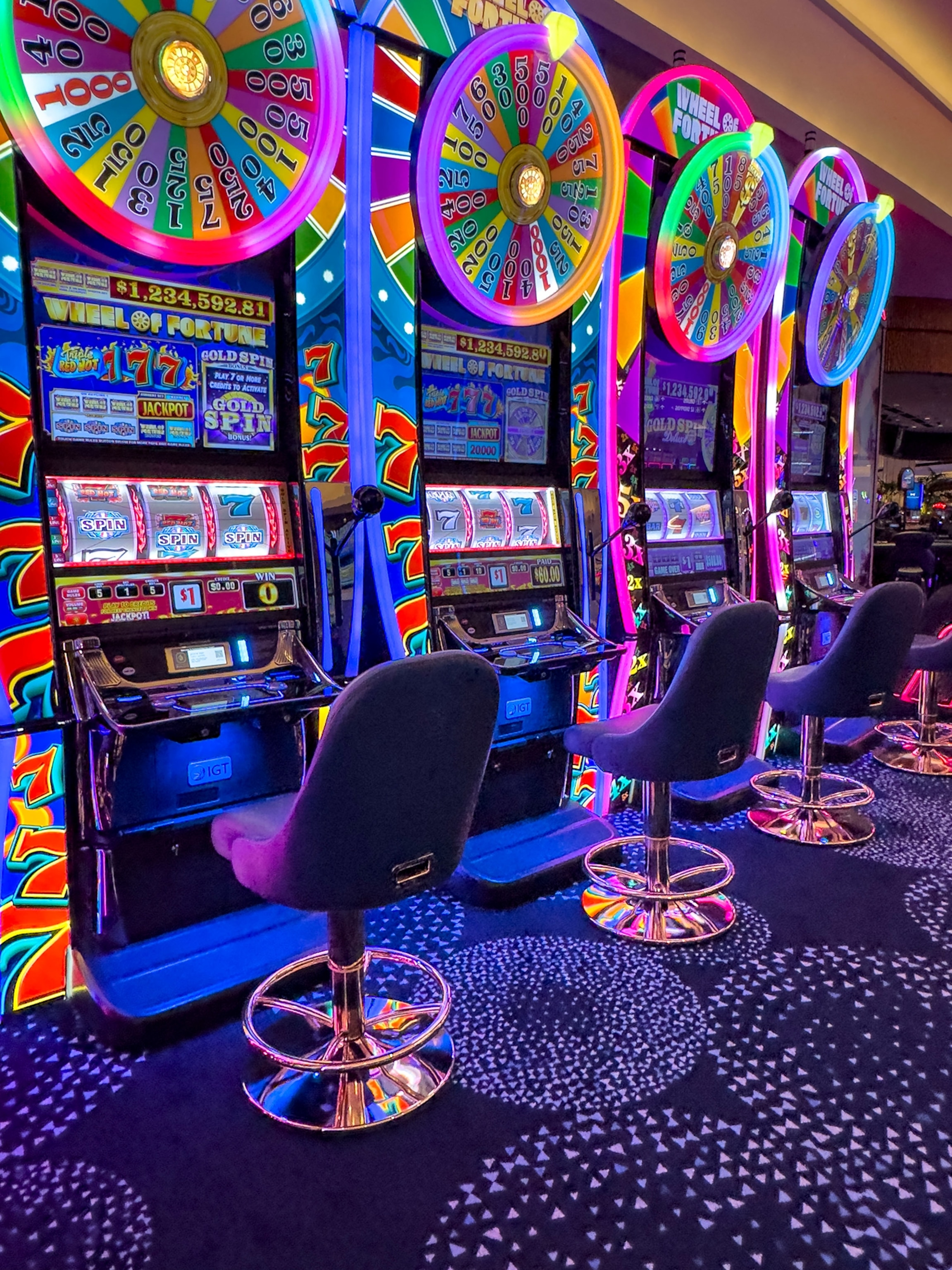 Soft purple seats are empty in front of the bright multi colored wheels of the slot machine.