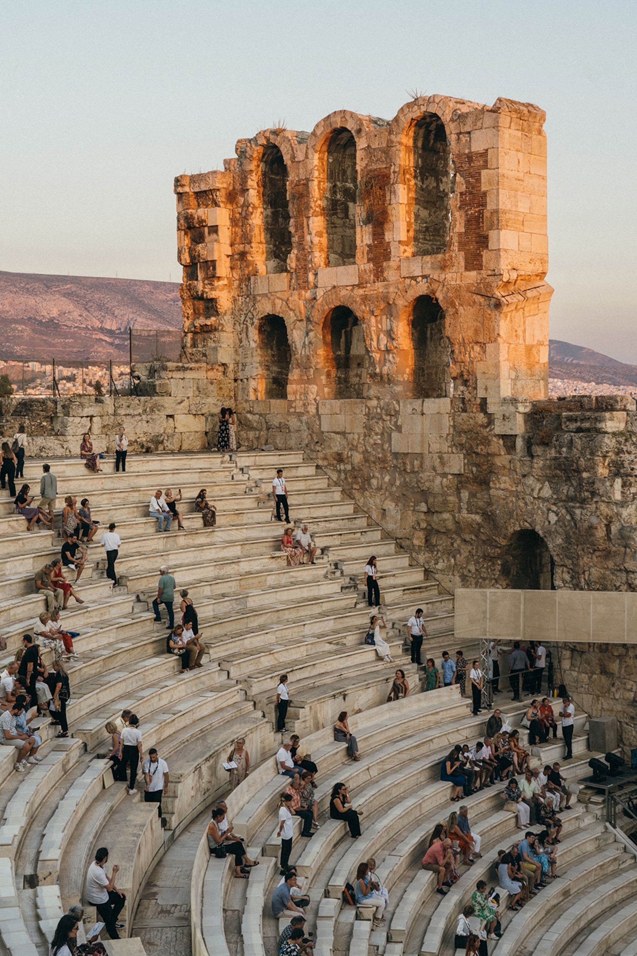 People sit on outdoor steps in the ruins of an old open air stone theatre