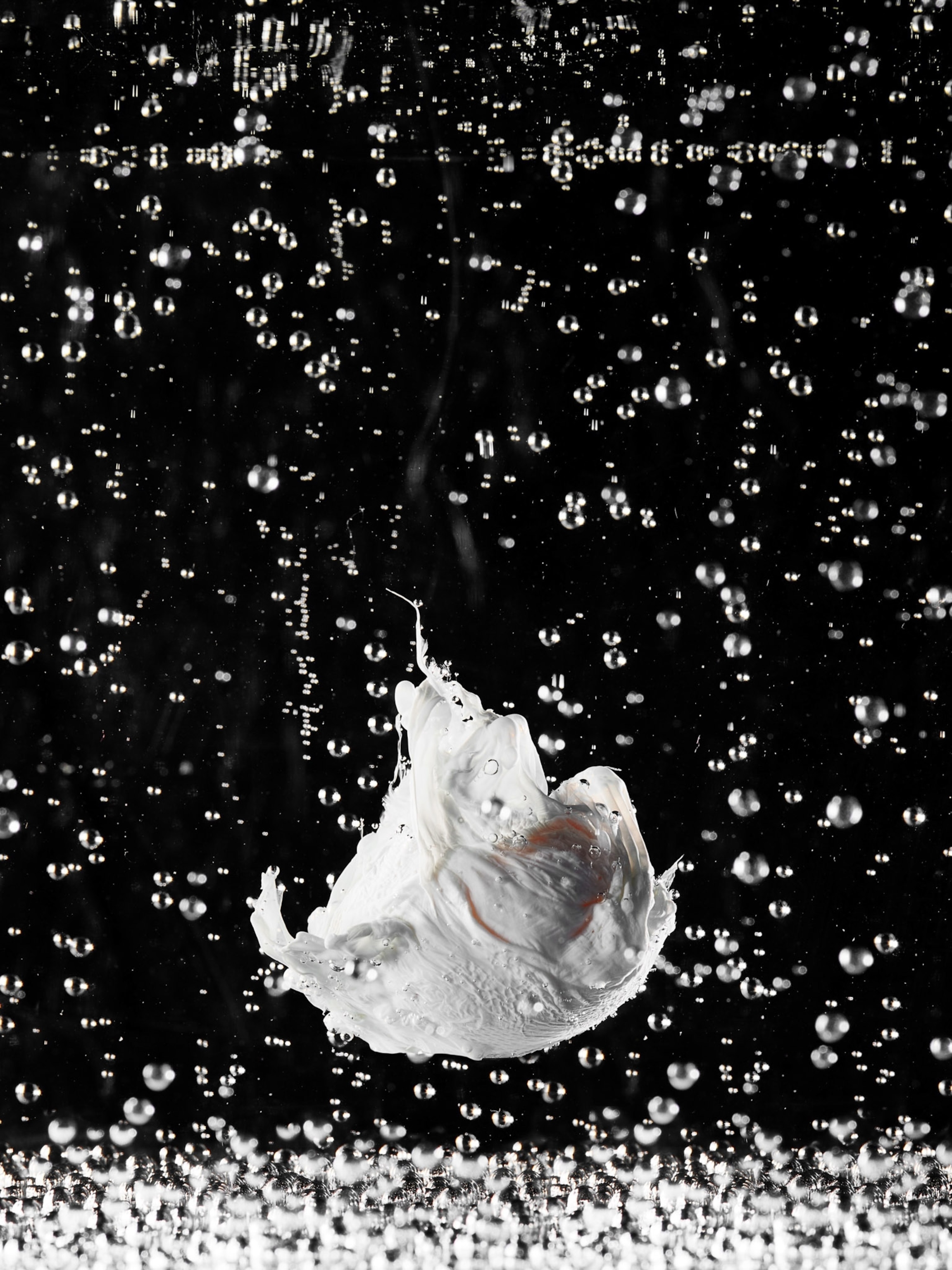 Egg falls to the bottom as bubbles float upward on a black background.