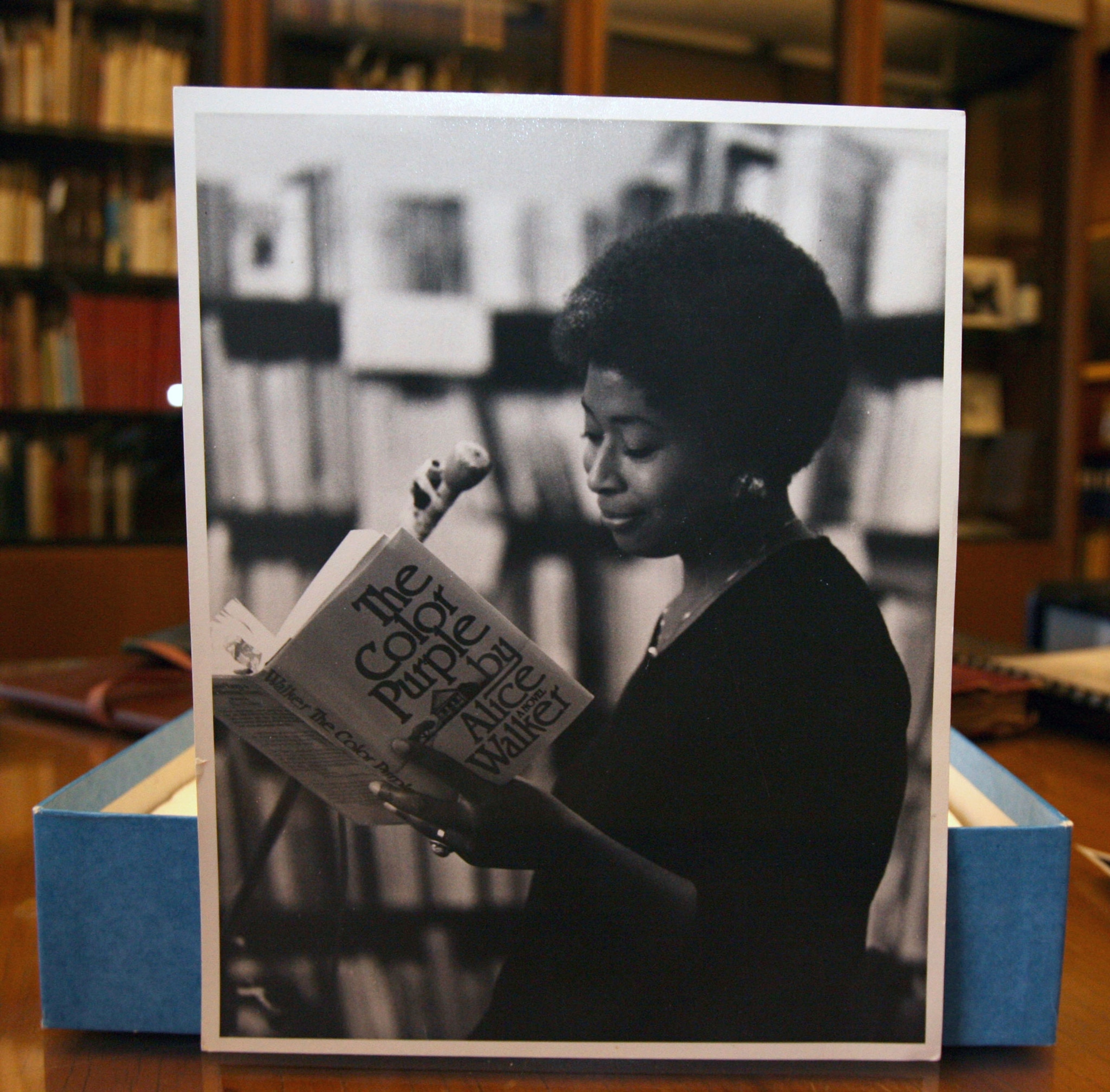 a black and white photograph of a woman reading a book at a microphone