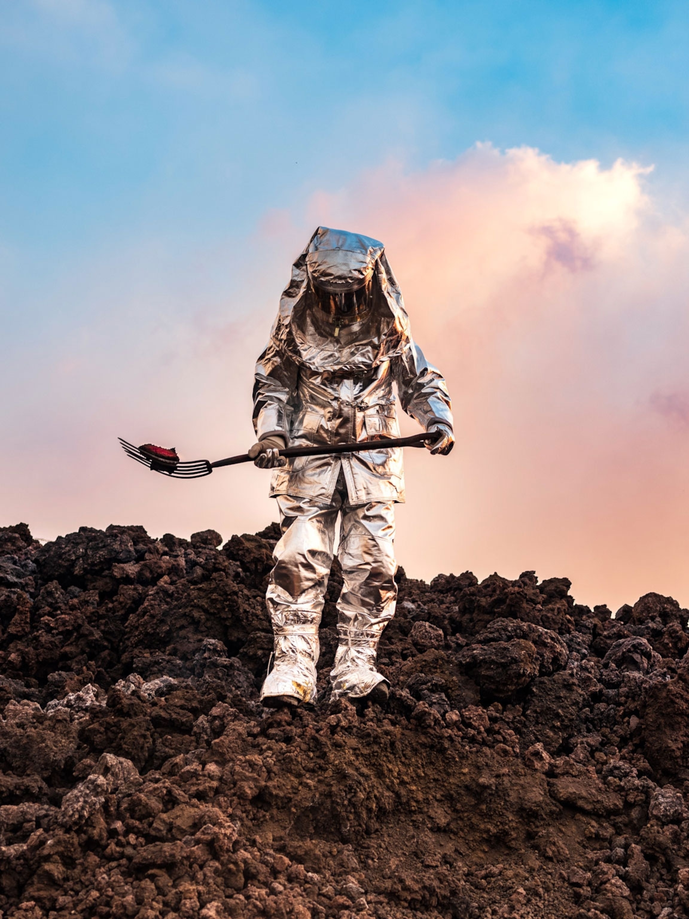 A person in a silver space suit collects samples among the rocky ground.