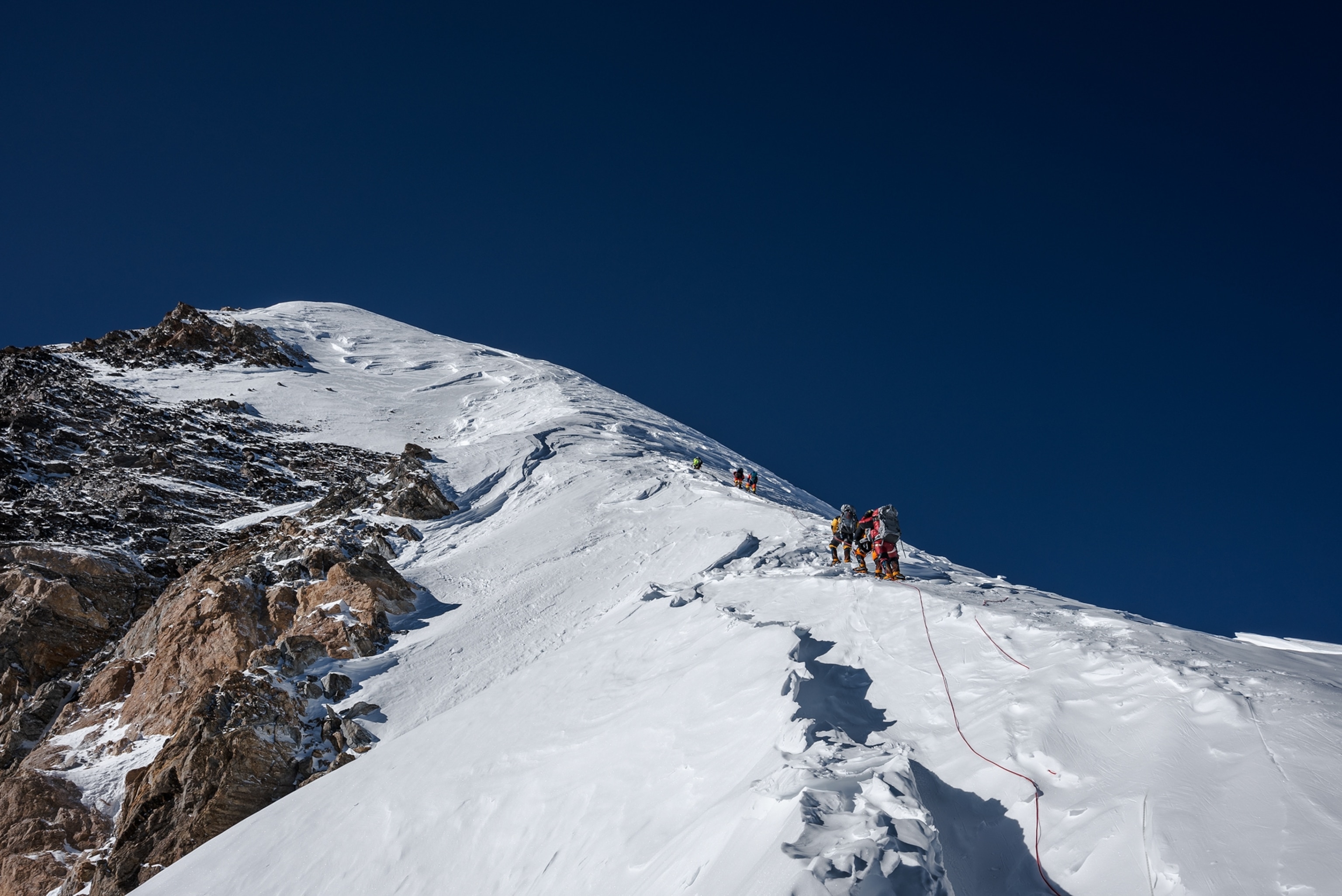 Picture of group of climbers spreading along rope on snowy slope few yards from mountaintop.