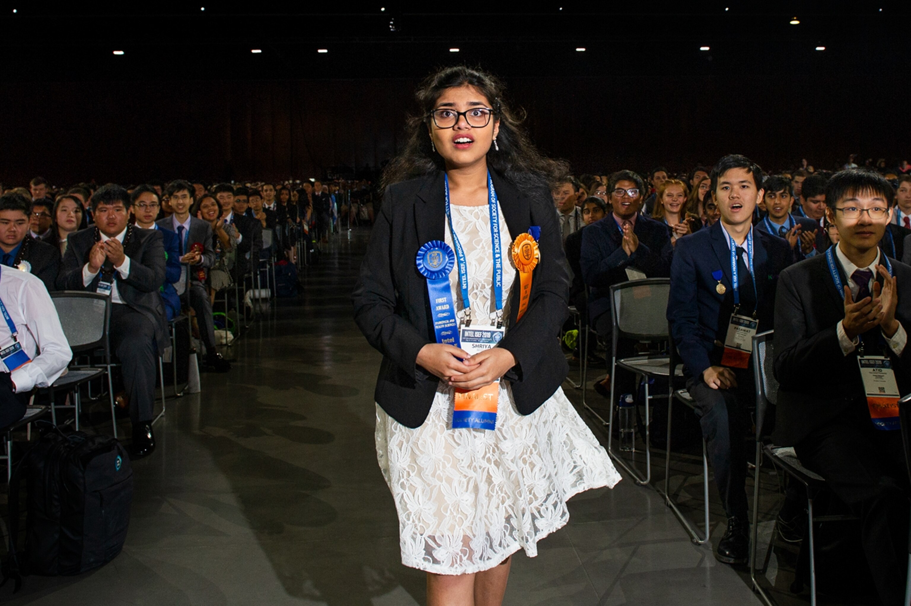 a young woman looking surprised as she walks down an auditorium isle