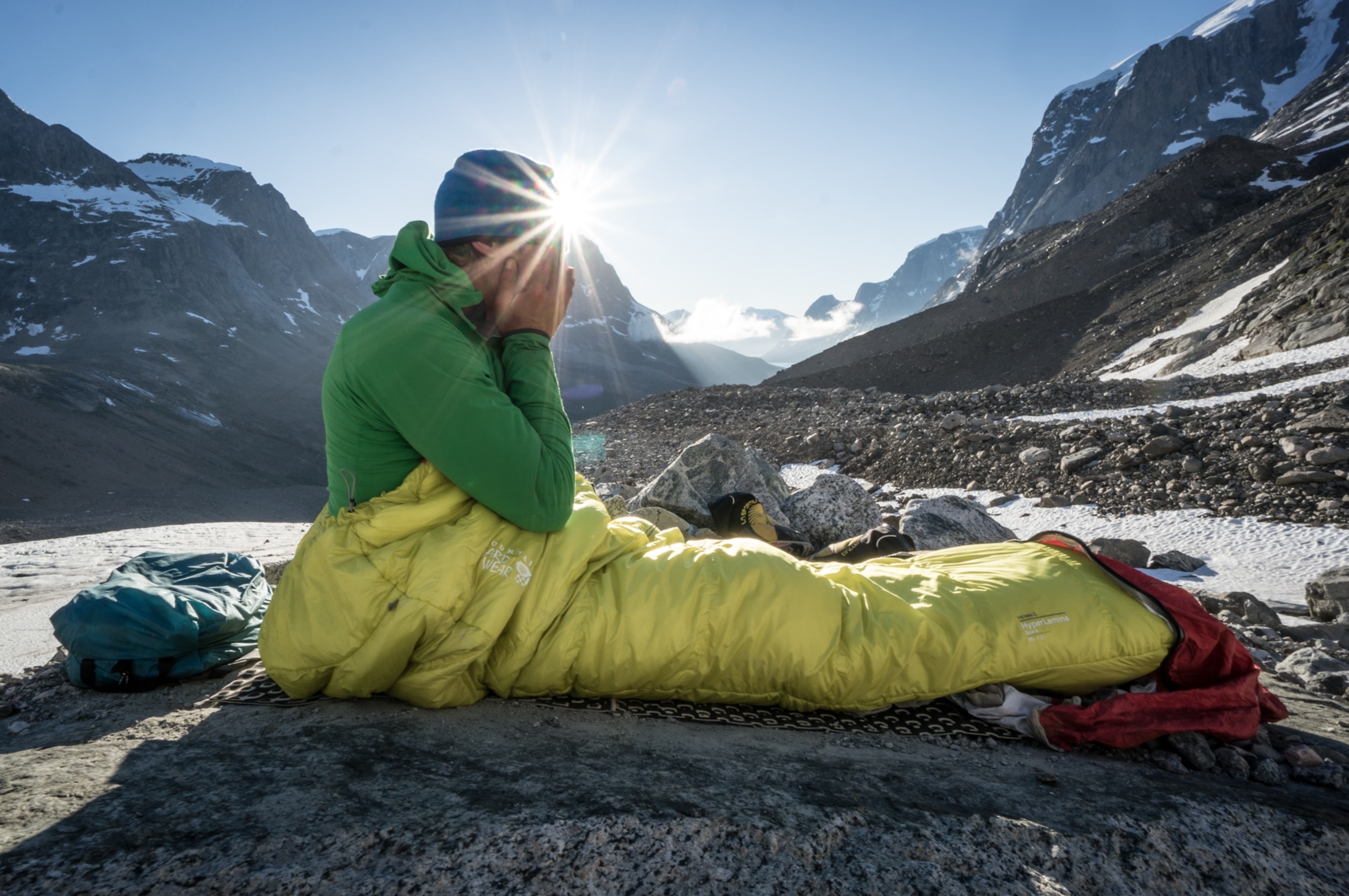 A hiker sits up in their sleeping bag after waking from a restful sleep along the Skjoldungen mountain range of Greenland.