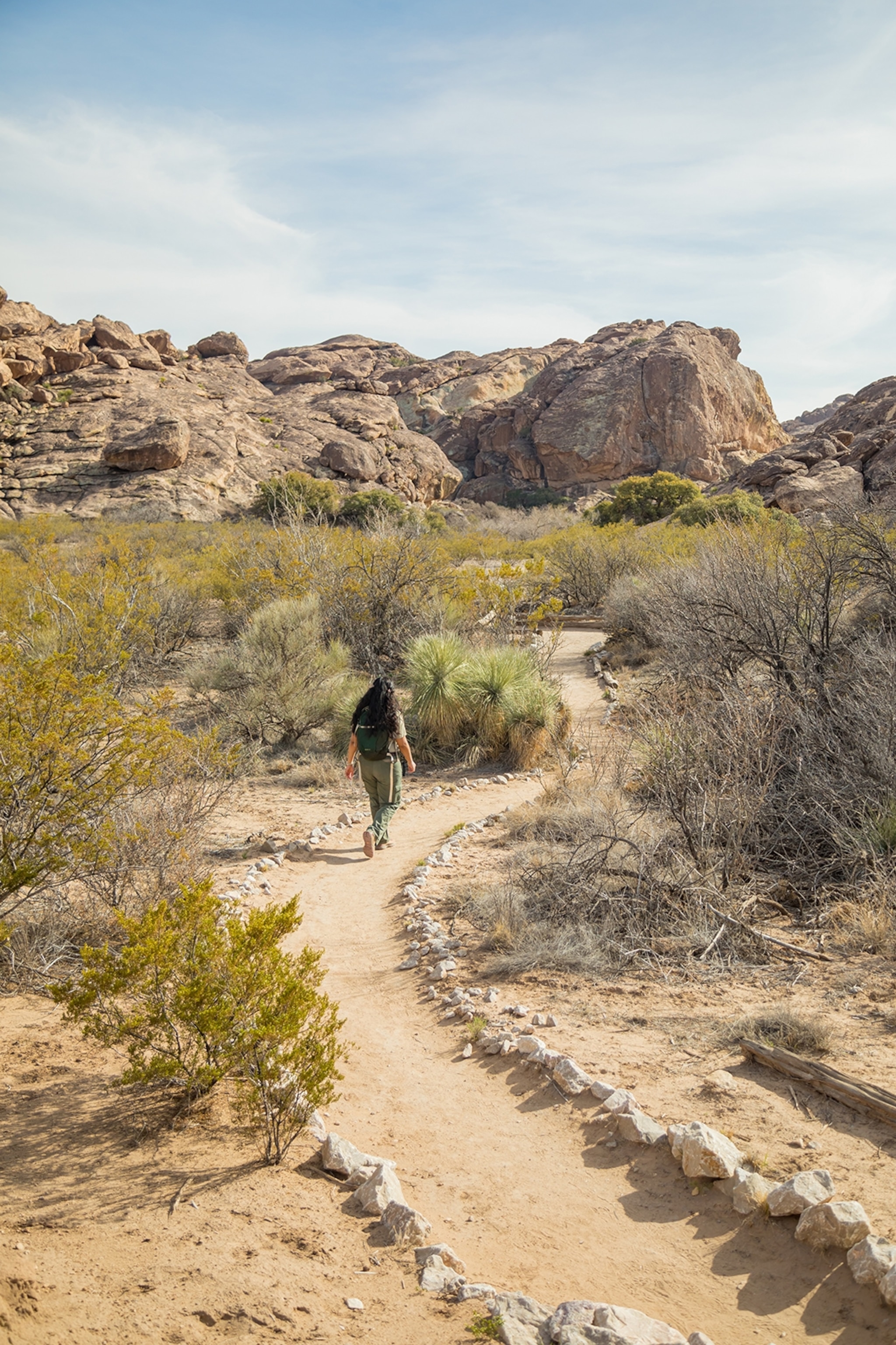 A person walking on a path surrounded by scrub in Hueco Tanks State Park and Historic Site, El Paso, Texas.