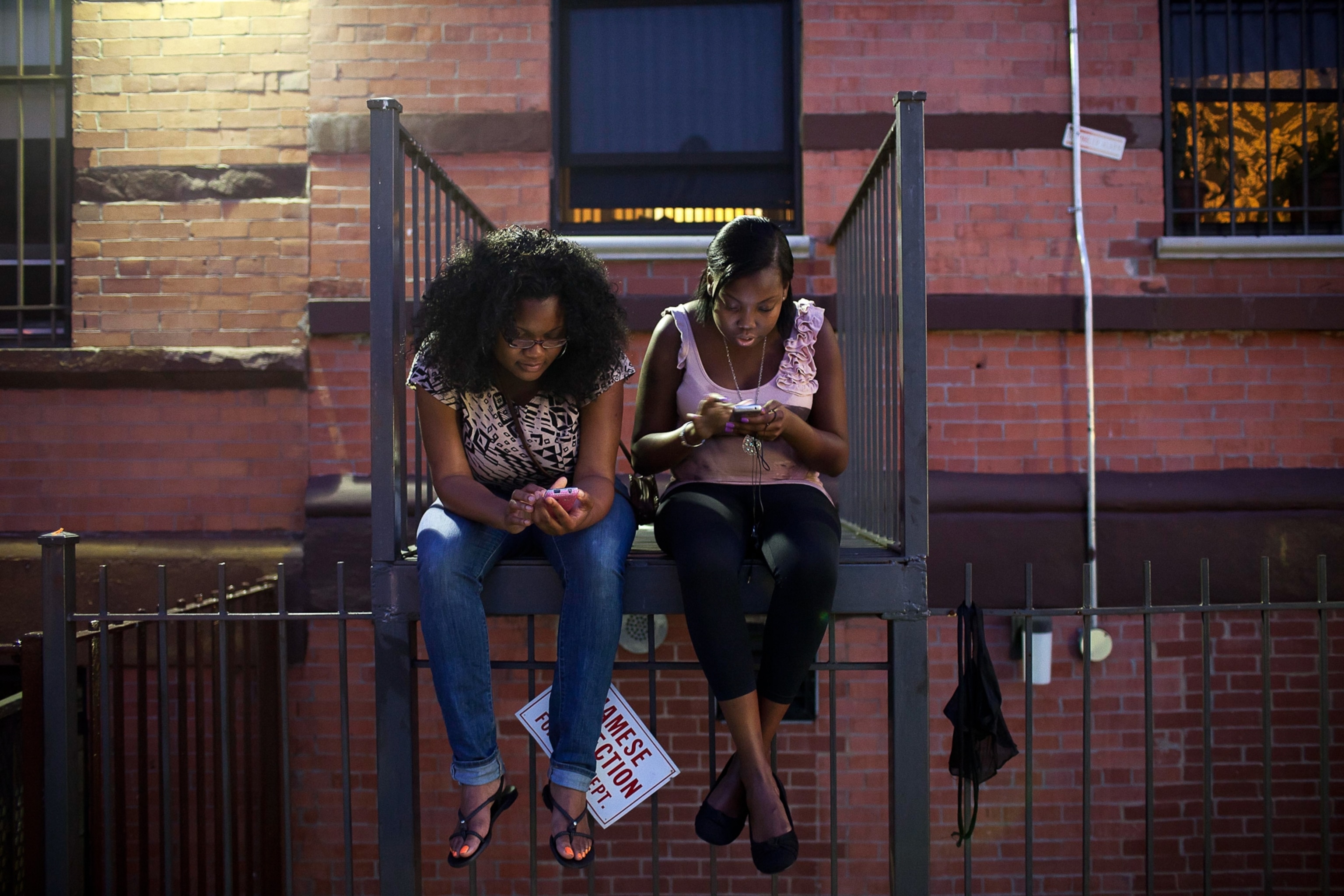Young girls check their phones on a fire escape.