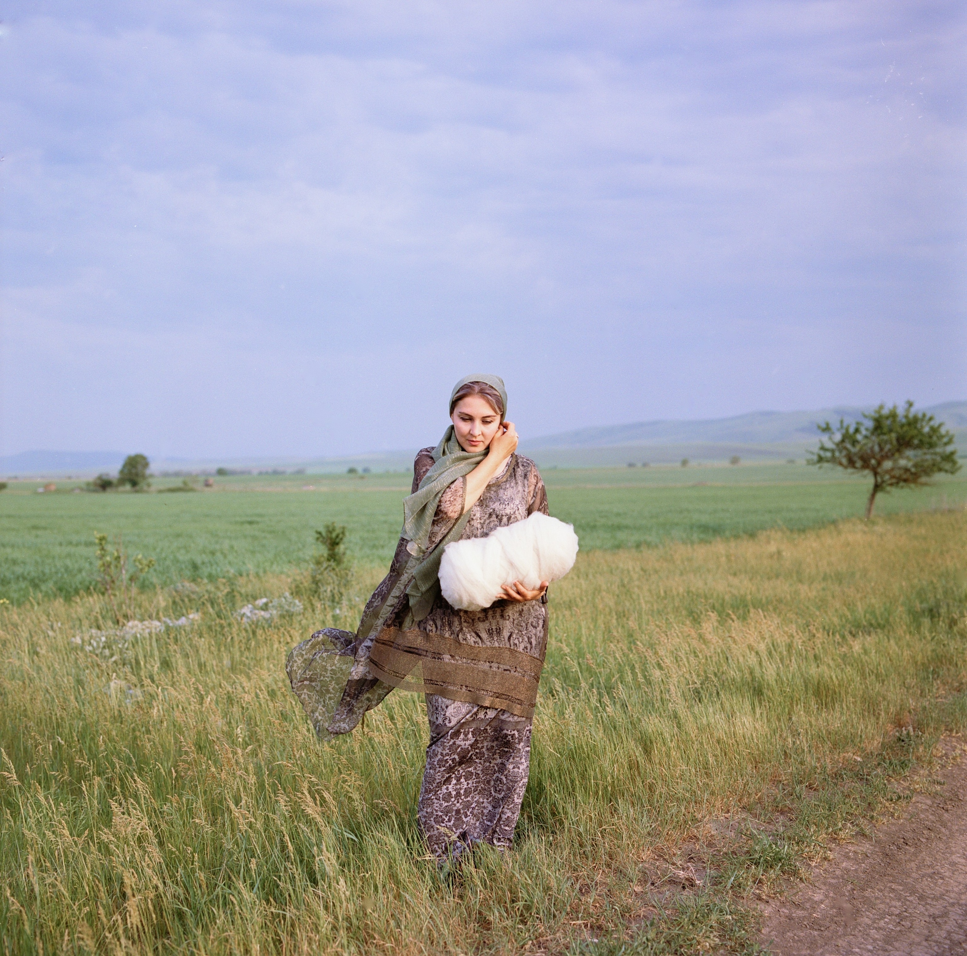 A woman in a field holds yarn used to make the felt rugs