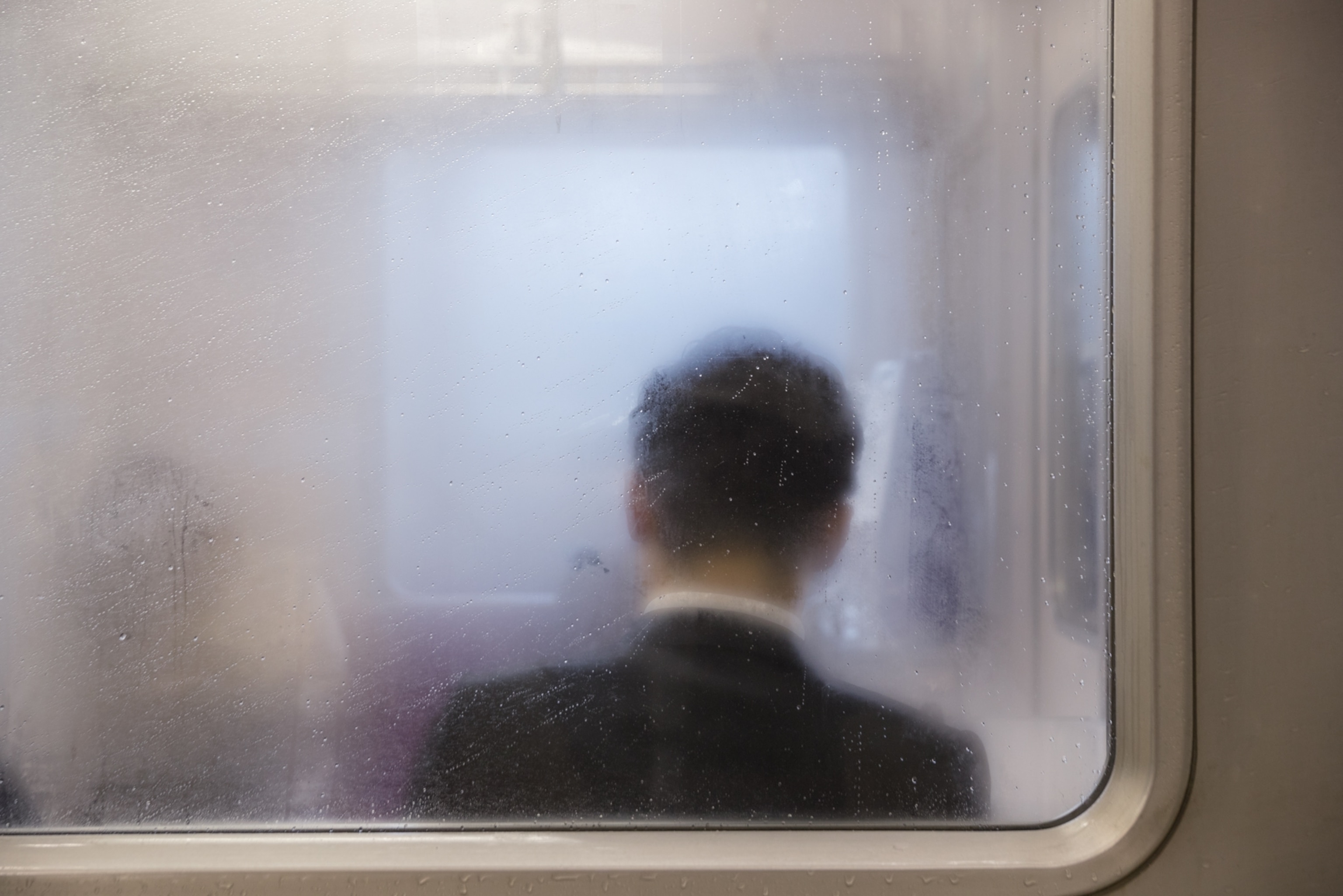 the back of a man sitting down through a foggy subway window