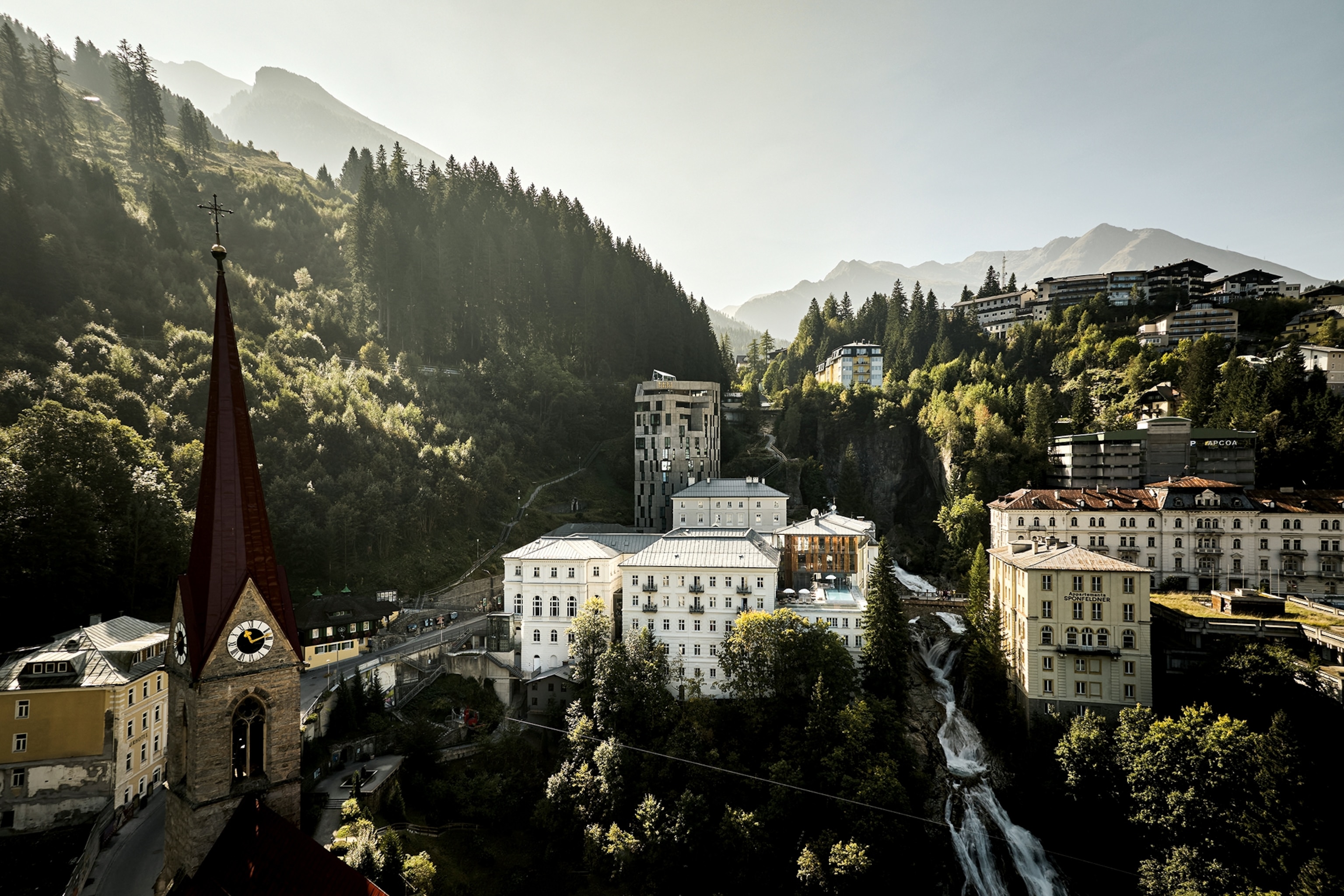 A far shot of a luxury resort in Austria. Buildings can be seen peaking through the tall trees.