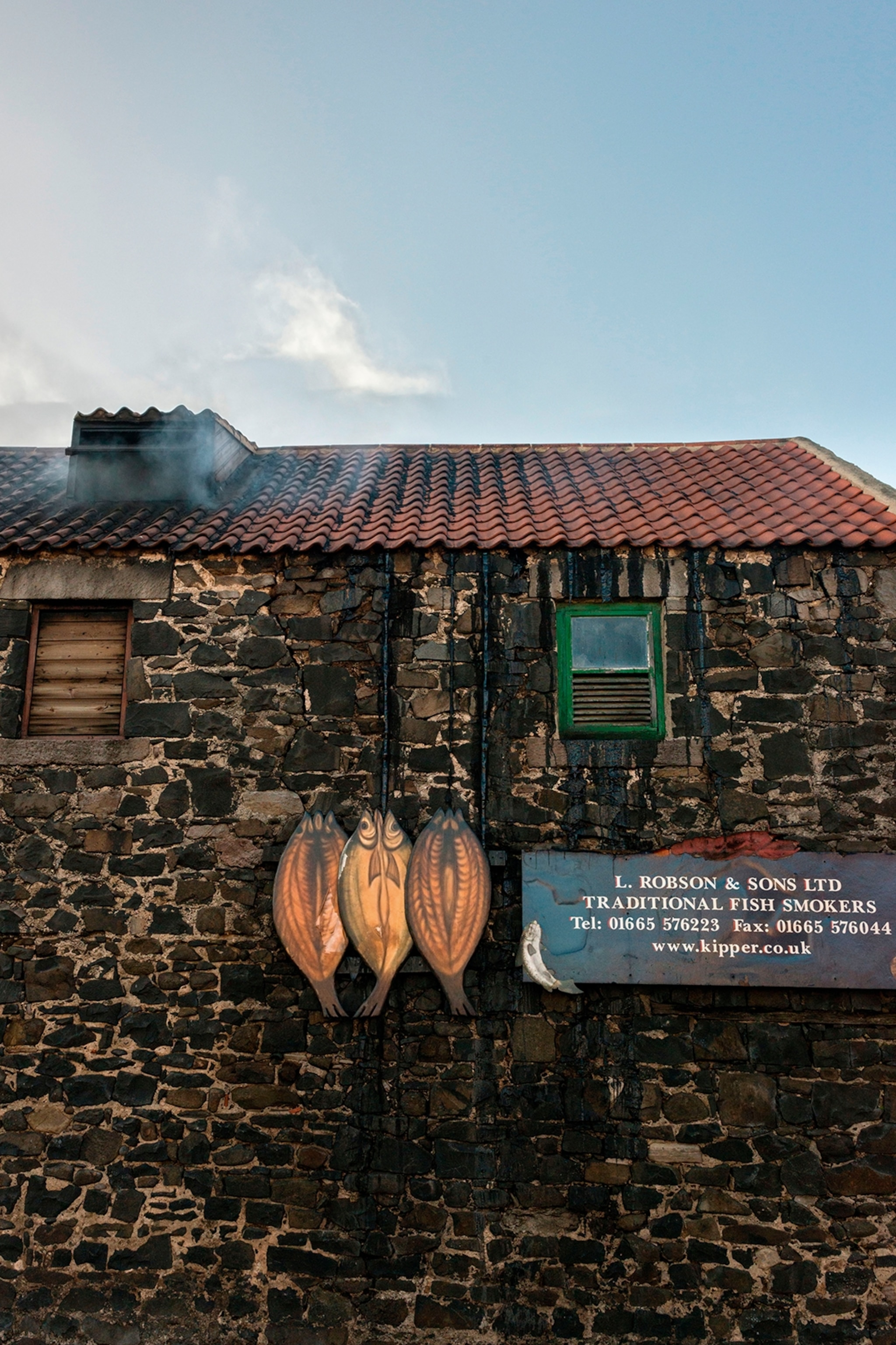 An old brick house with smoke escaping one of the chimneys, smoked wooden fish plates hung on the facade.