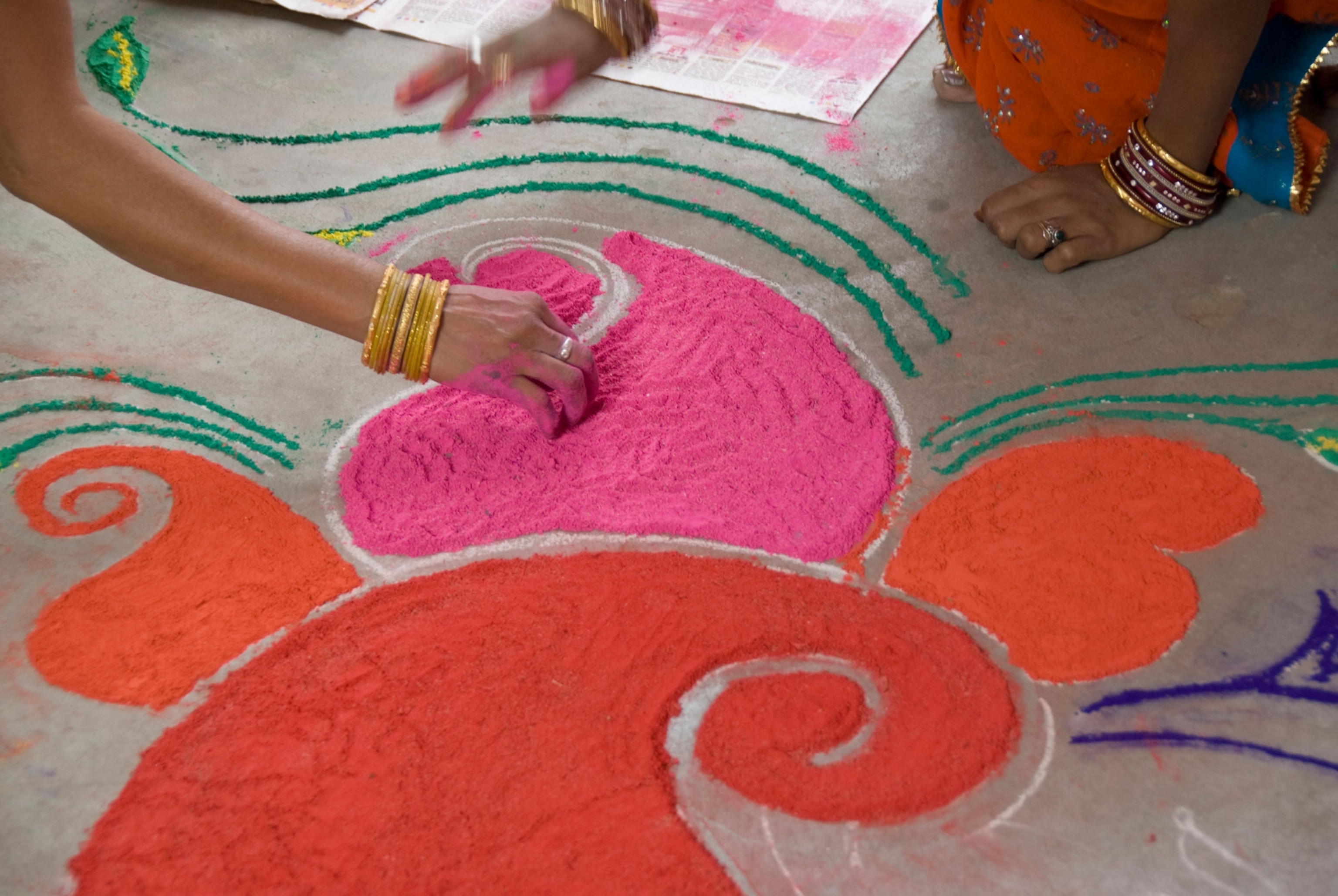 People make designs on a floor using colorful sand