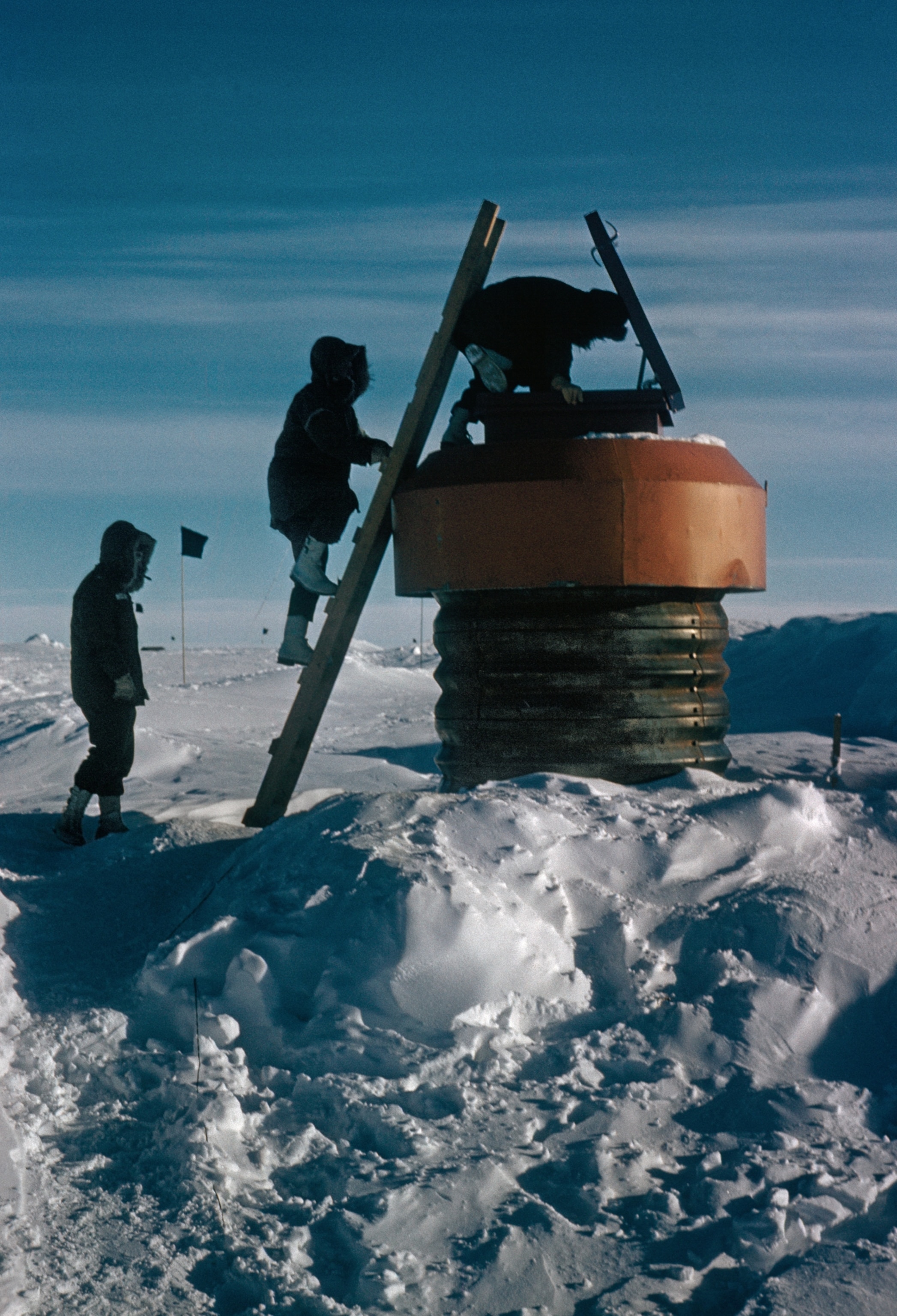 Two workers are pictured outside in the snow testing one of the polar station’s 15 escape hatches. One worker is halfway up the ladder, and the other is at the foot.
