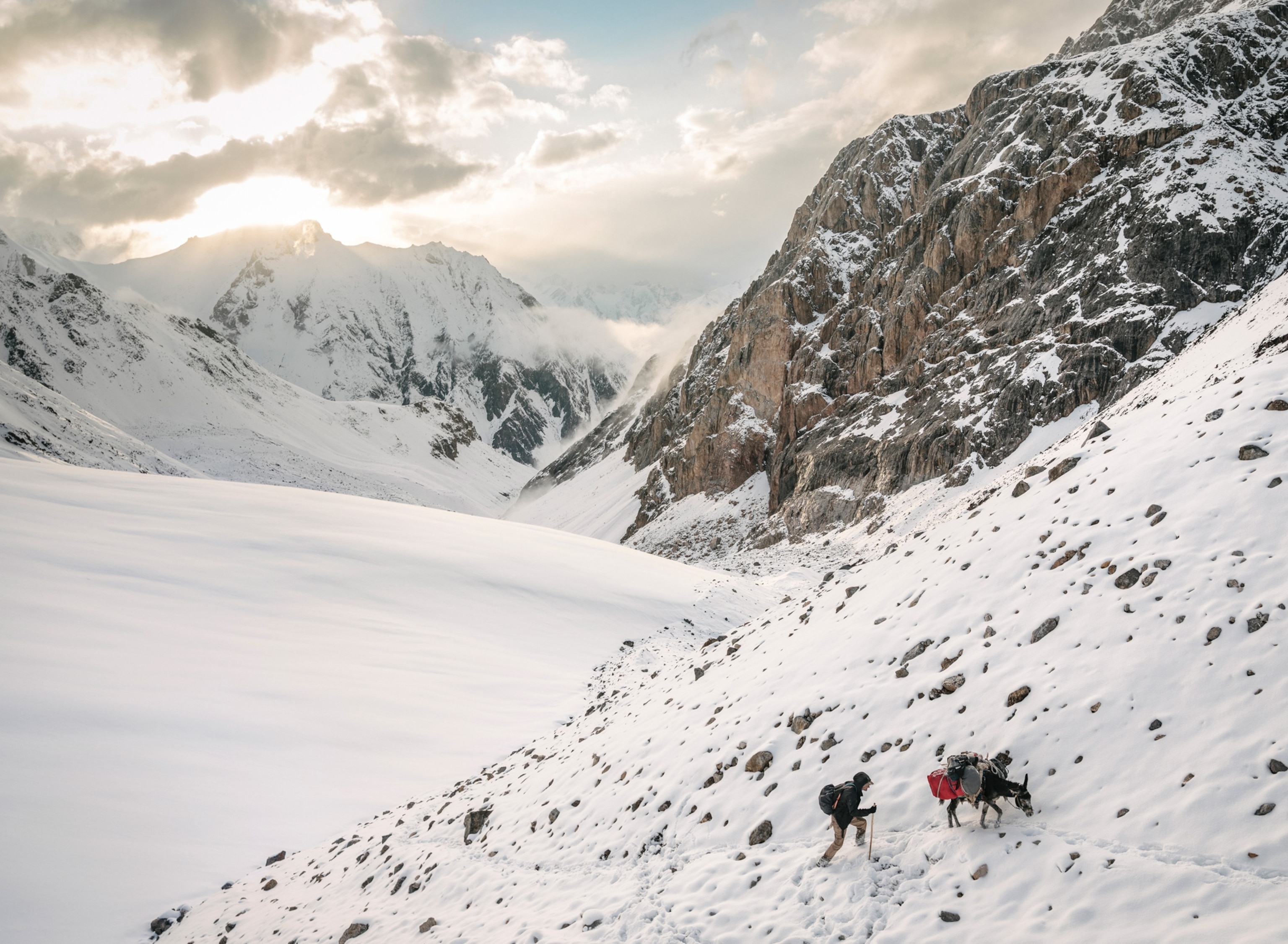 Photo of man and donkey trekking through a snow covered mountain