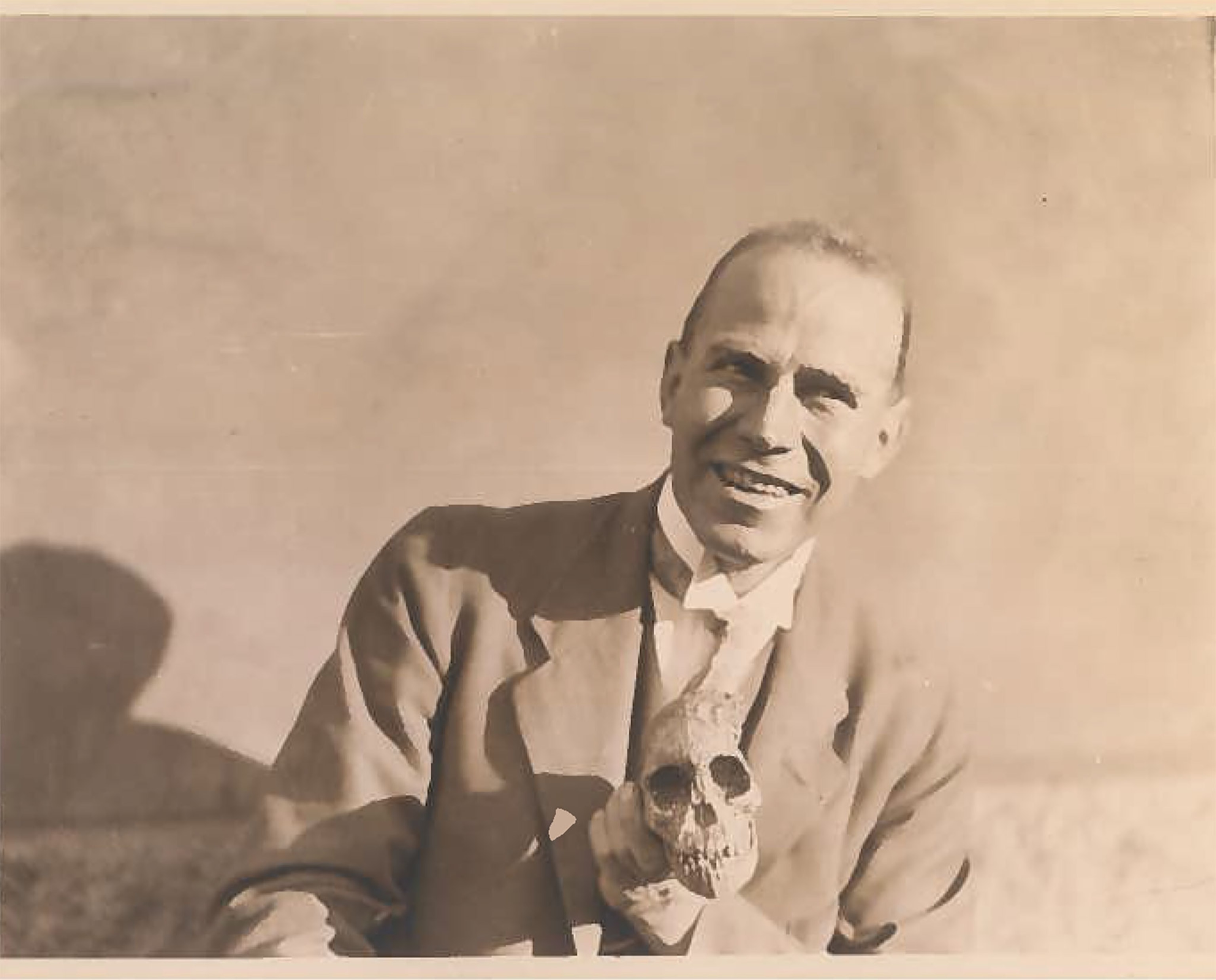 Black and white photo of an anthropologist holding a small human skull.