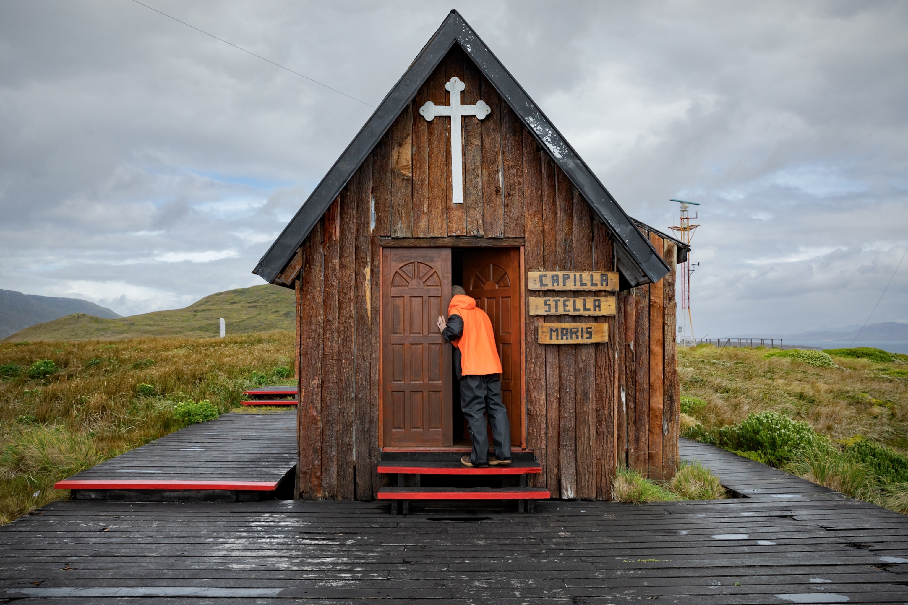 Picture of man in orange jacket picking into small wooden chapel.