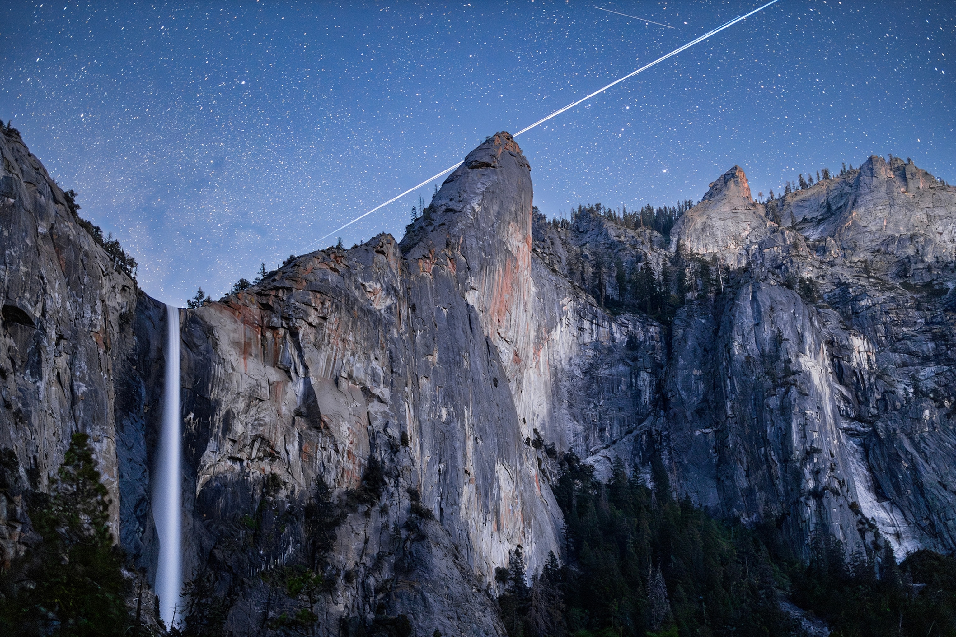 Long exposure view of Starlink satellites streaking over Bridalveil Fall and Cathedral Rock in Yosemite.