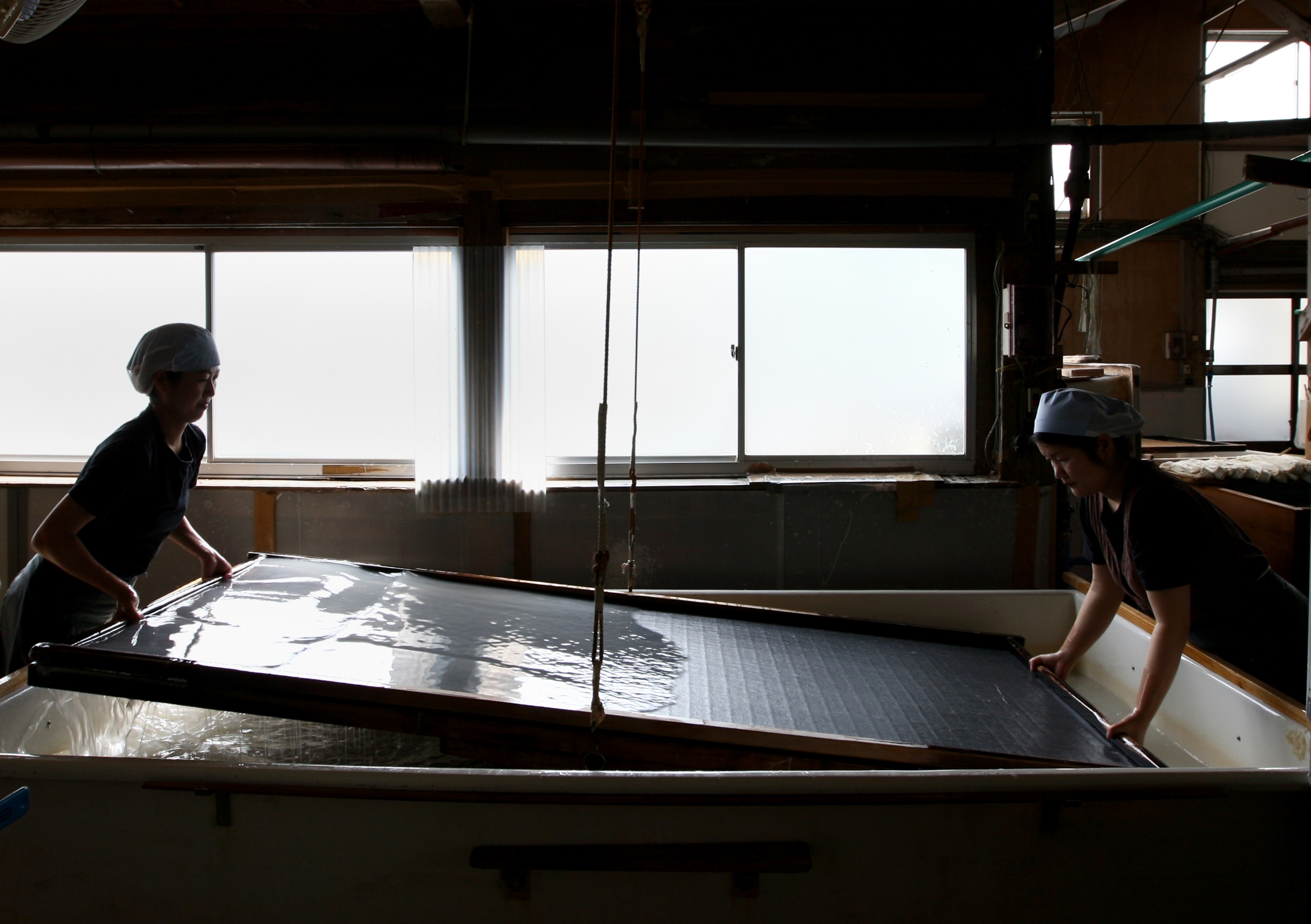 Workers filter pulp at a mill that produces handmade washi paper
